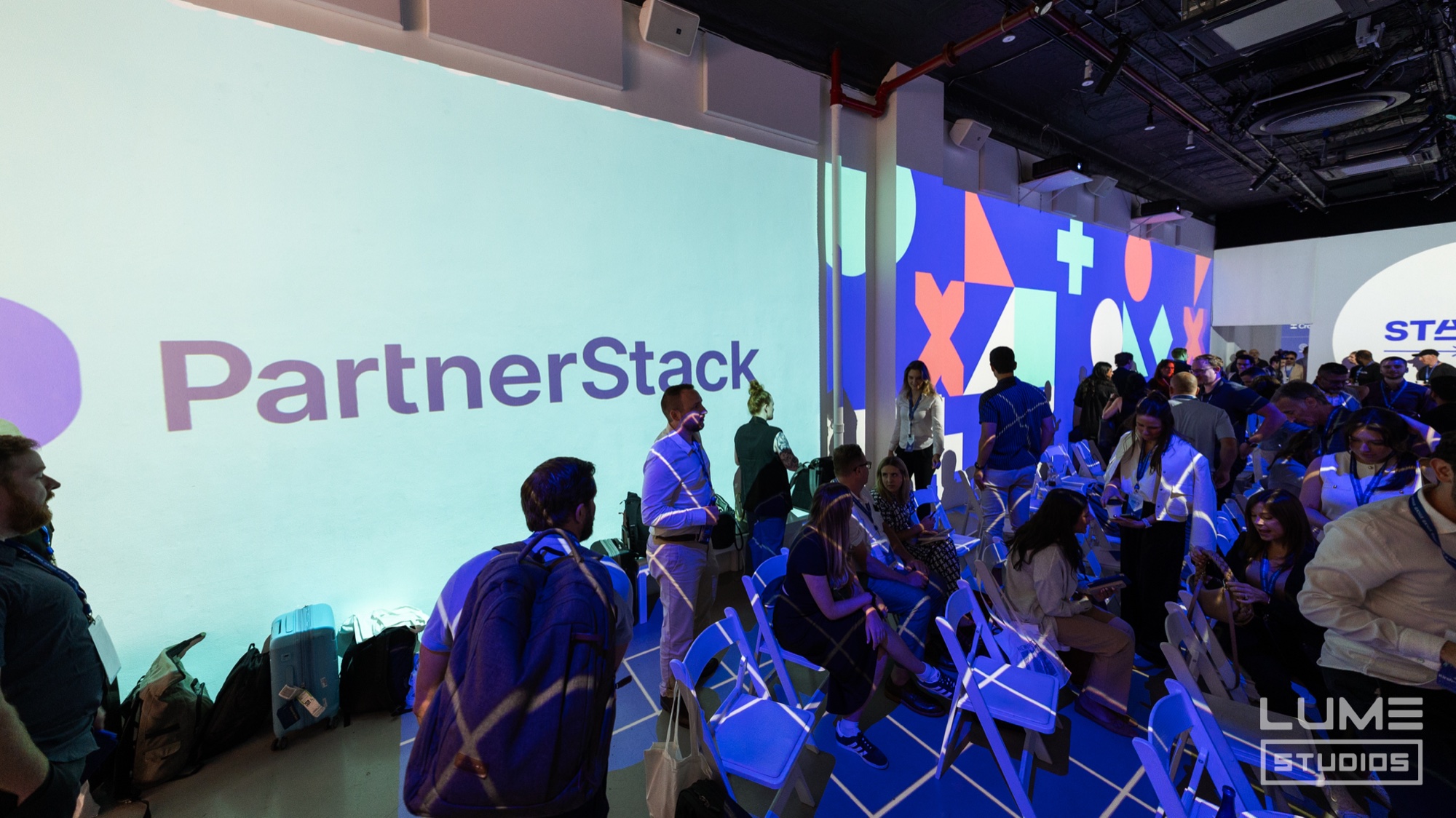 PartnerStack logo projected across a pale wall while guests take their seats under blue light at Lume Studios