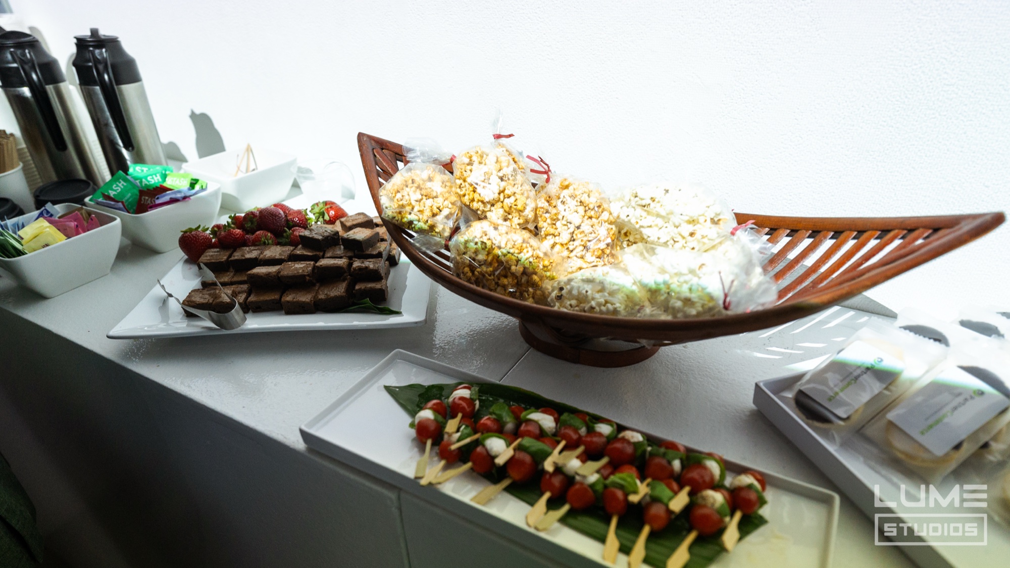 Snack station with bagged popcorn in a wooden bowl, caprese skewers, brownies and coffee dispensers