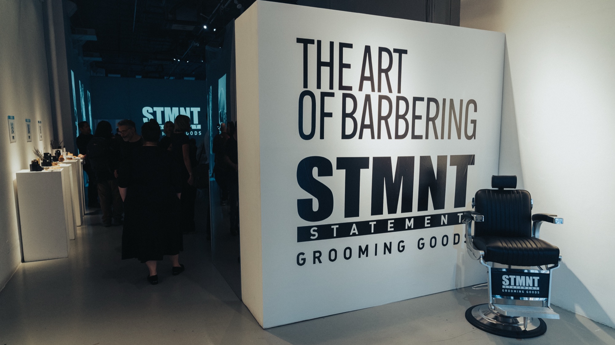A white wall reading The Art of Barbering STMNT Grooming Goods beside a black leather barber chair