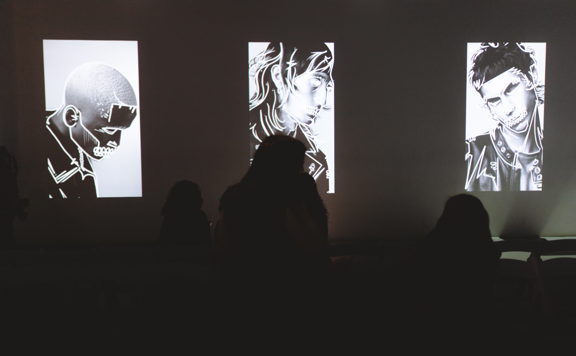 Silhouetted audience watches three tall screens with black and white line drawings of styled men