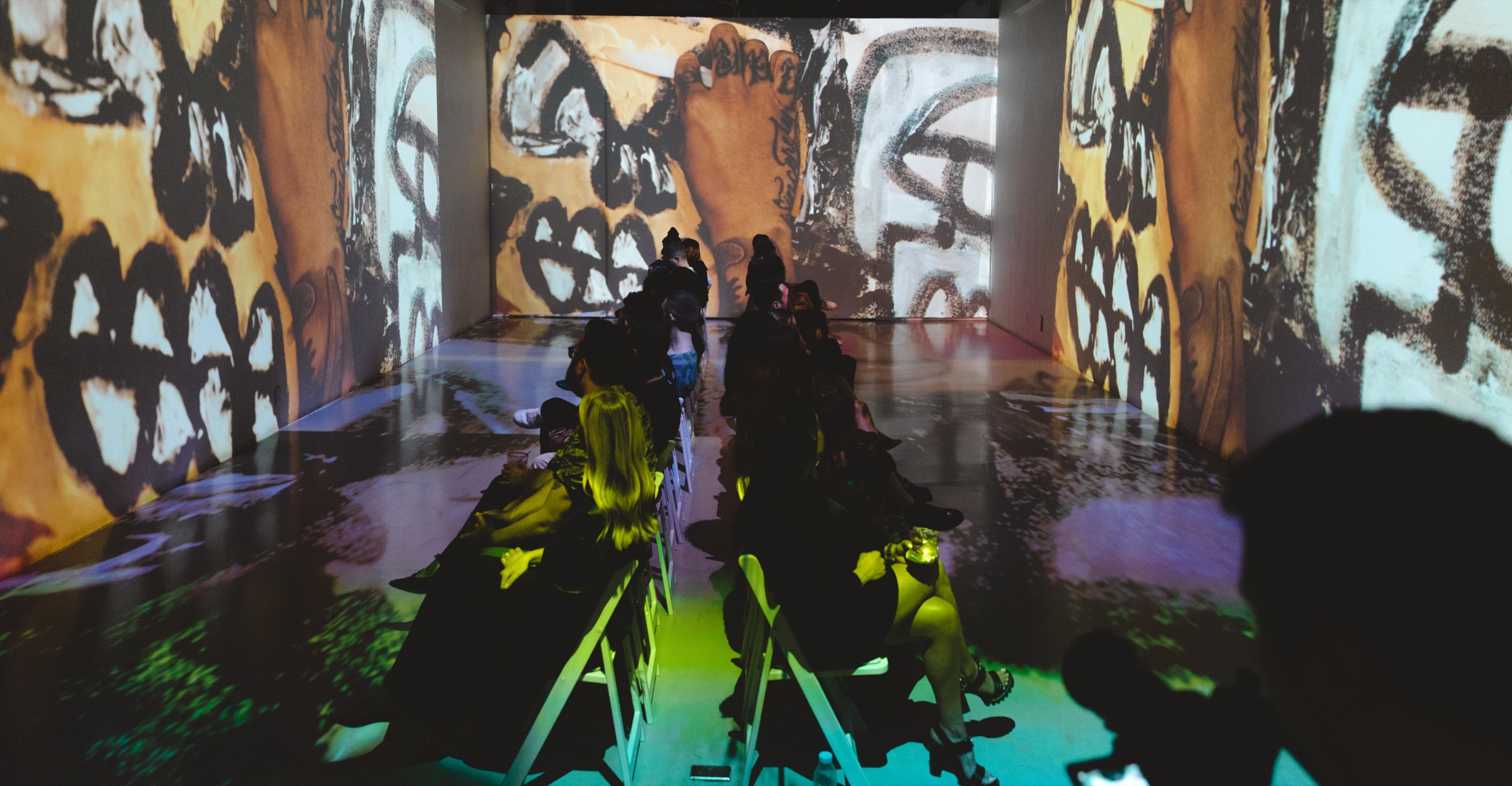 Guests seated in a corridor projected floor to ceiling with orange and black scrawled skull drawings