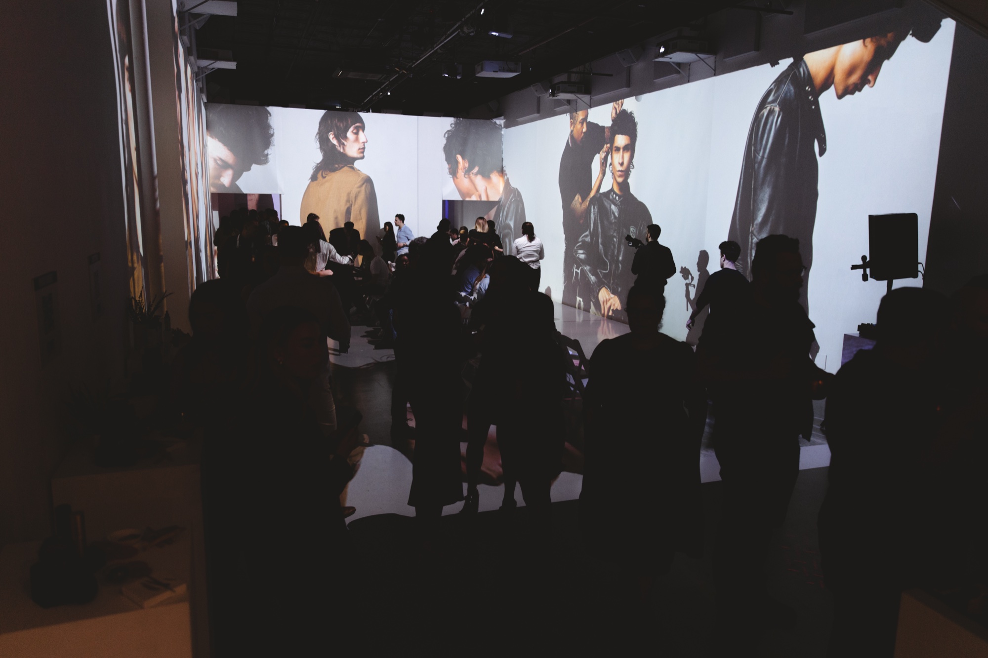 Silhouetted crowd before floor to ceiling projections of a dark haired model in a leather jacket