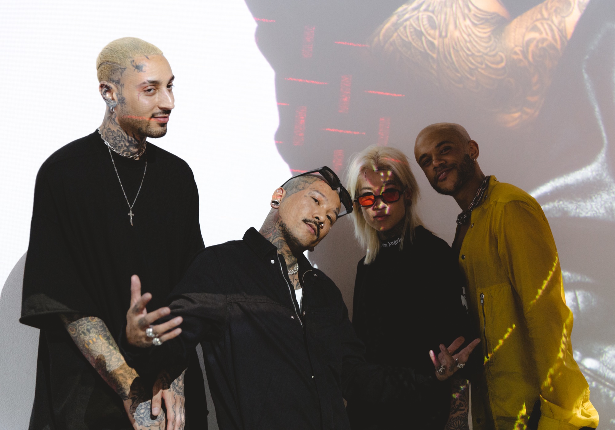 Four people in black and yellow posing before a projection, two with bleached hair and tattoos