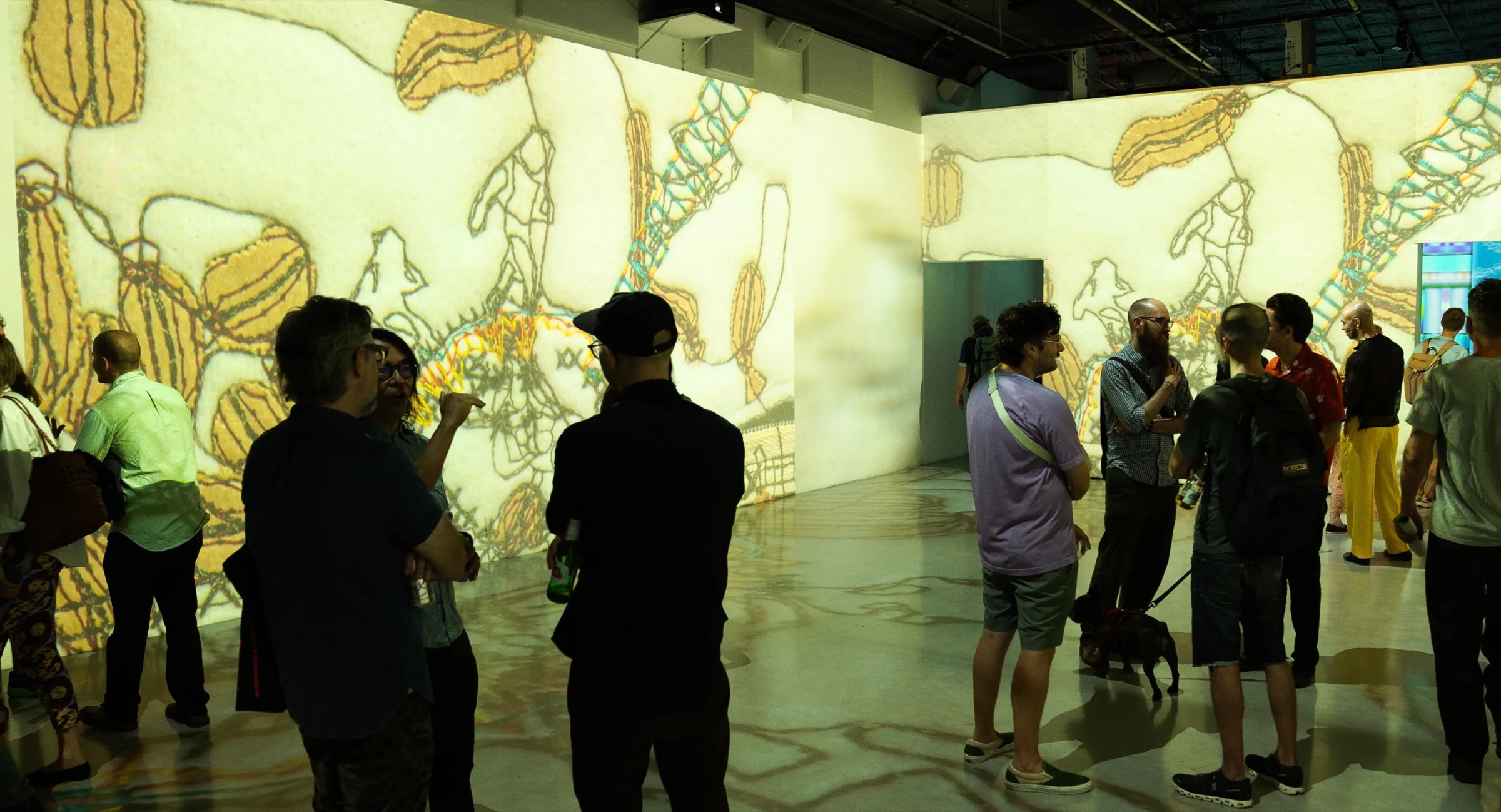 Guests stand in the Lume immersive studio as sketched figures and warm color wash the walls and floor