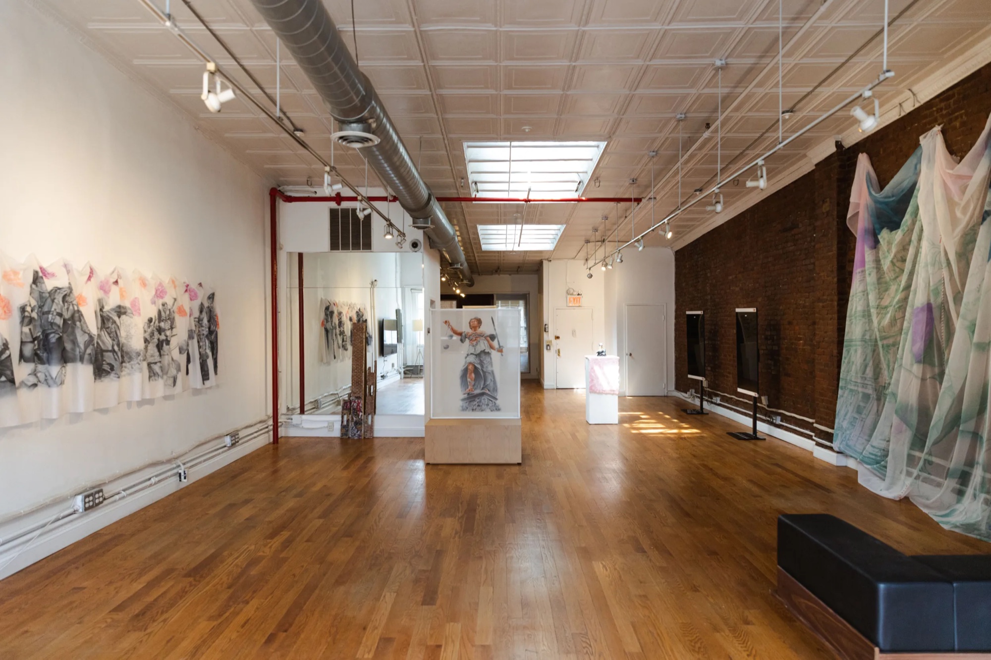 Daylight loft at Lume Studios hung with textile works, a pedestal sculpture, and screens along the brick wall