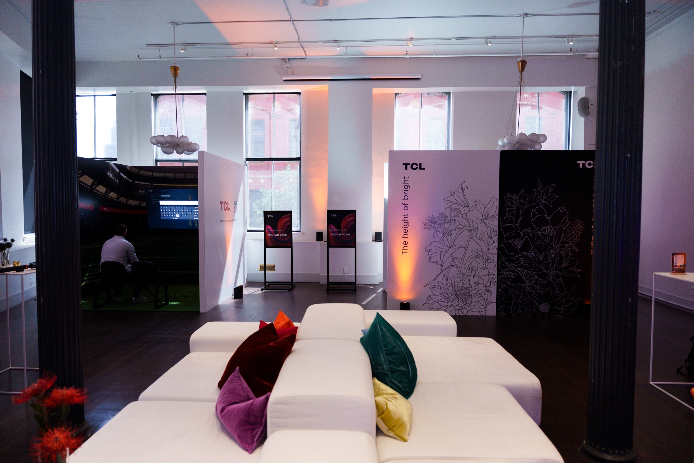 White sectional sofa with jewel toned cushions in a loft with TCL panels and warm orange window light