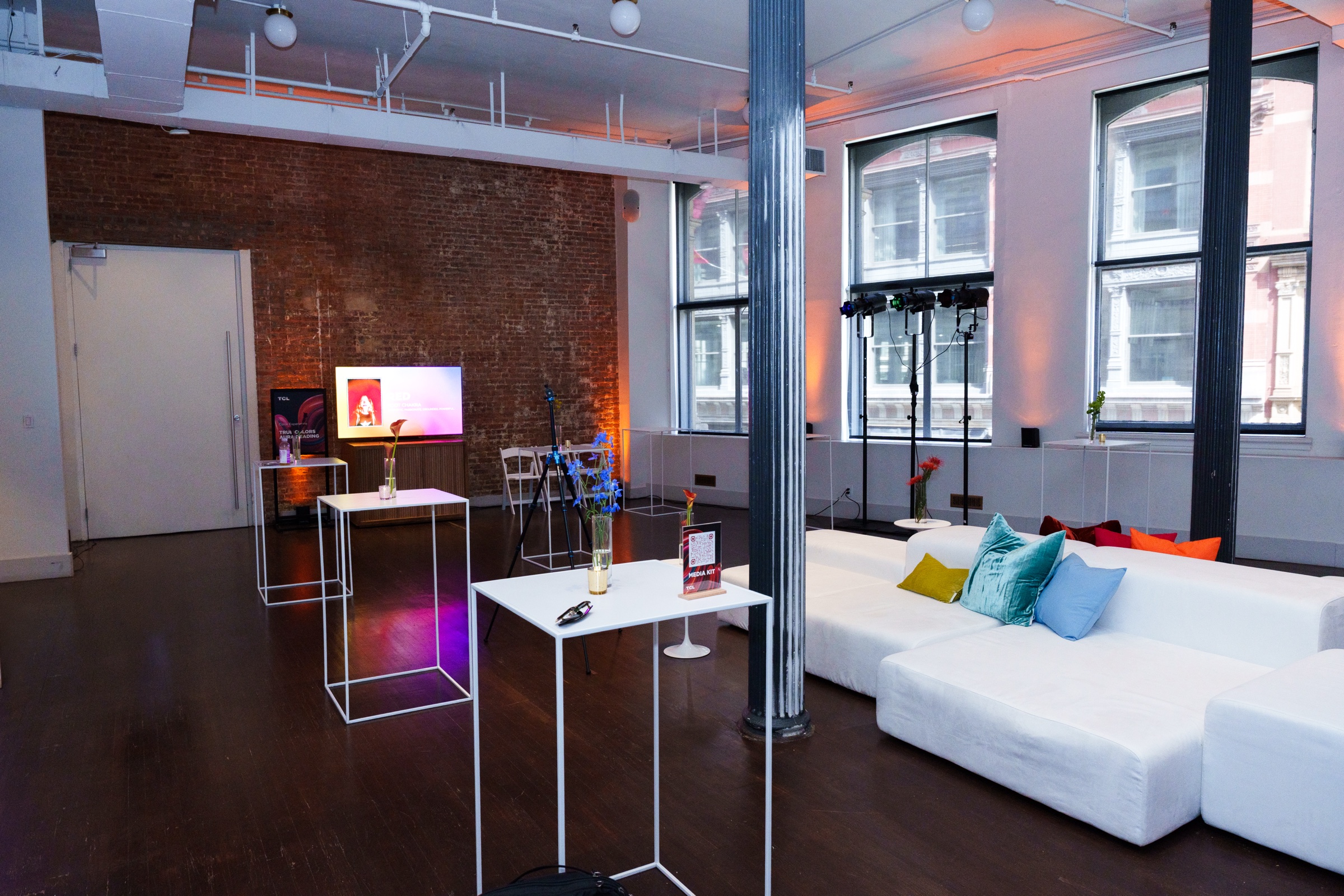 Brick loft lounge with a white sectional sofa, colourful cushions, tall white side tables and a screen
