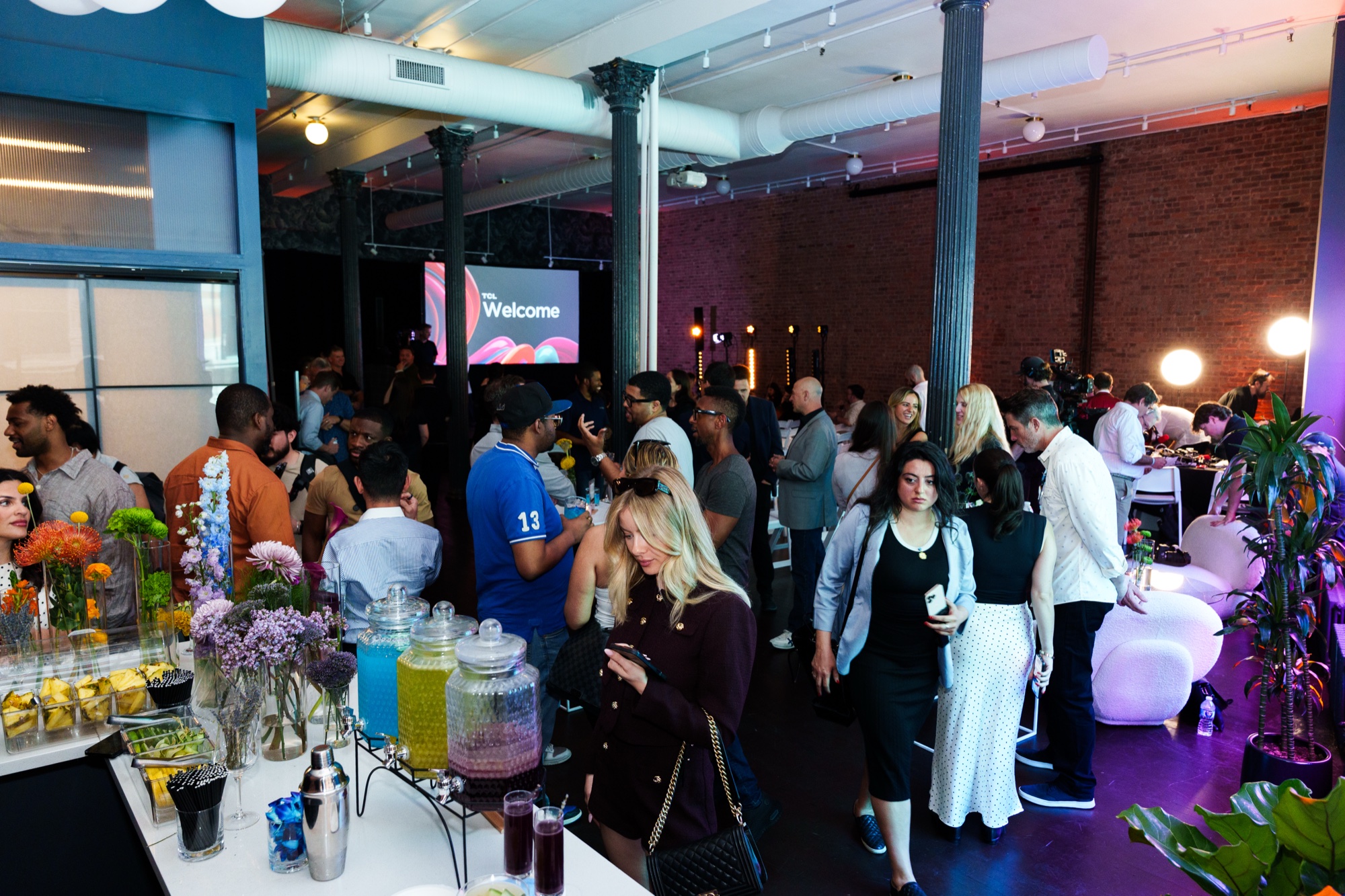 Crowded brick loft with a Welcome screen, flowers and drink jars on a bar in the foreground