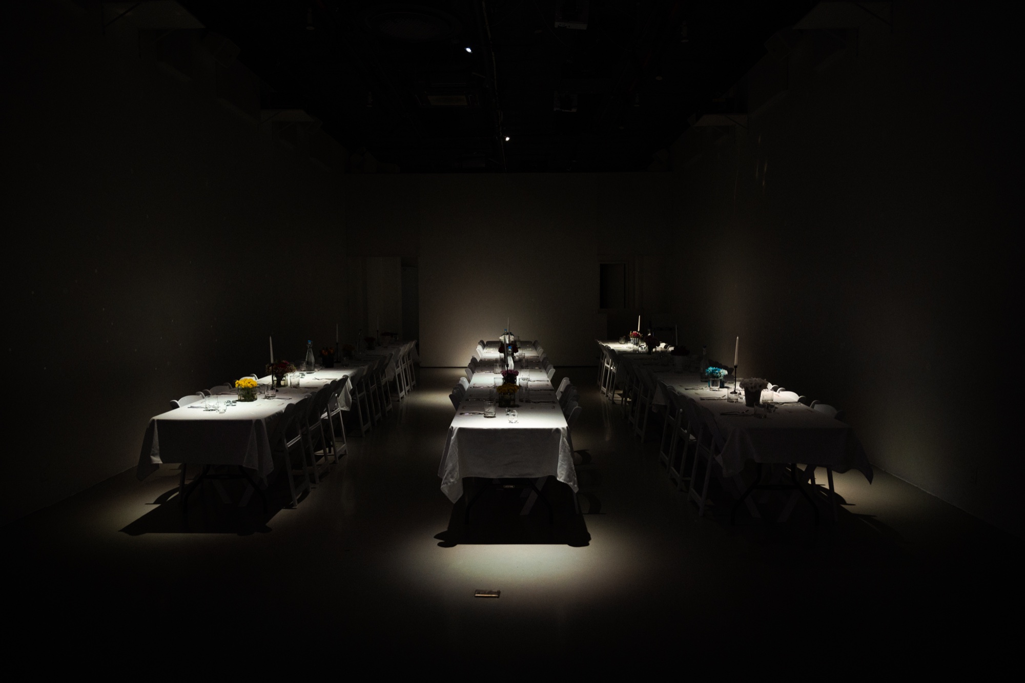 Empty white banquet tables spotlit with flowers and candles before guests arrive