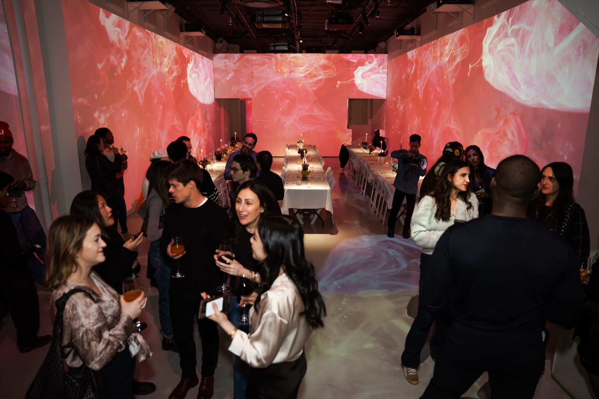 Guests hold wine glasses in a room where pink and white marbled patterns are projected on every wall