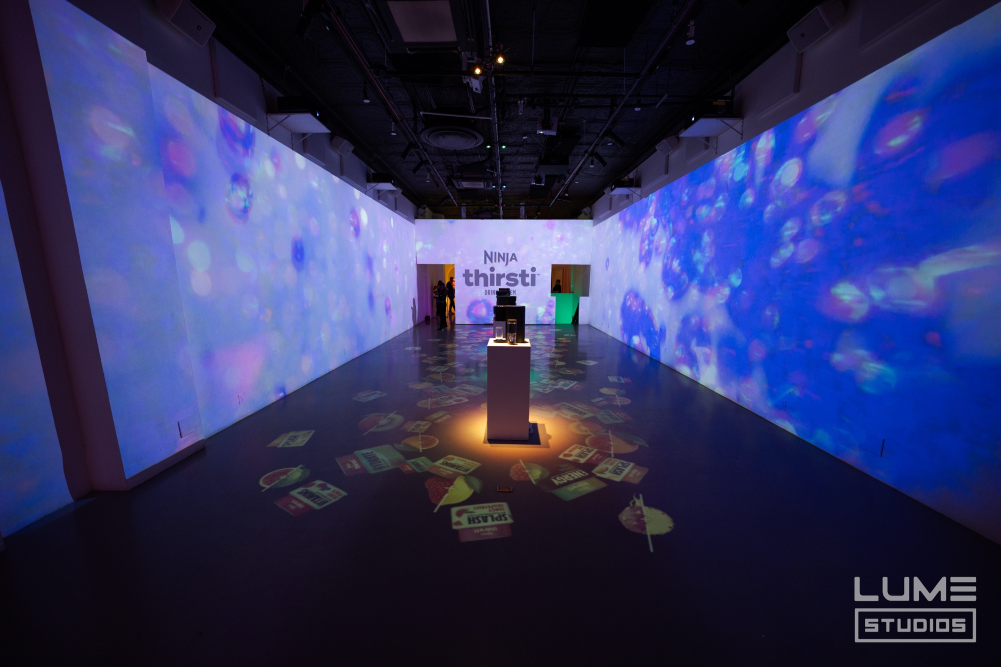 Mirrored coolers filled with glowing teal, pink, and yellow bottles sit beneath a sign reading “thousands of drinks”
