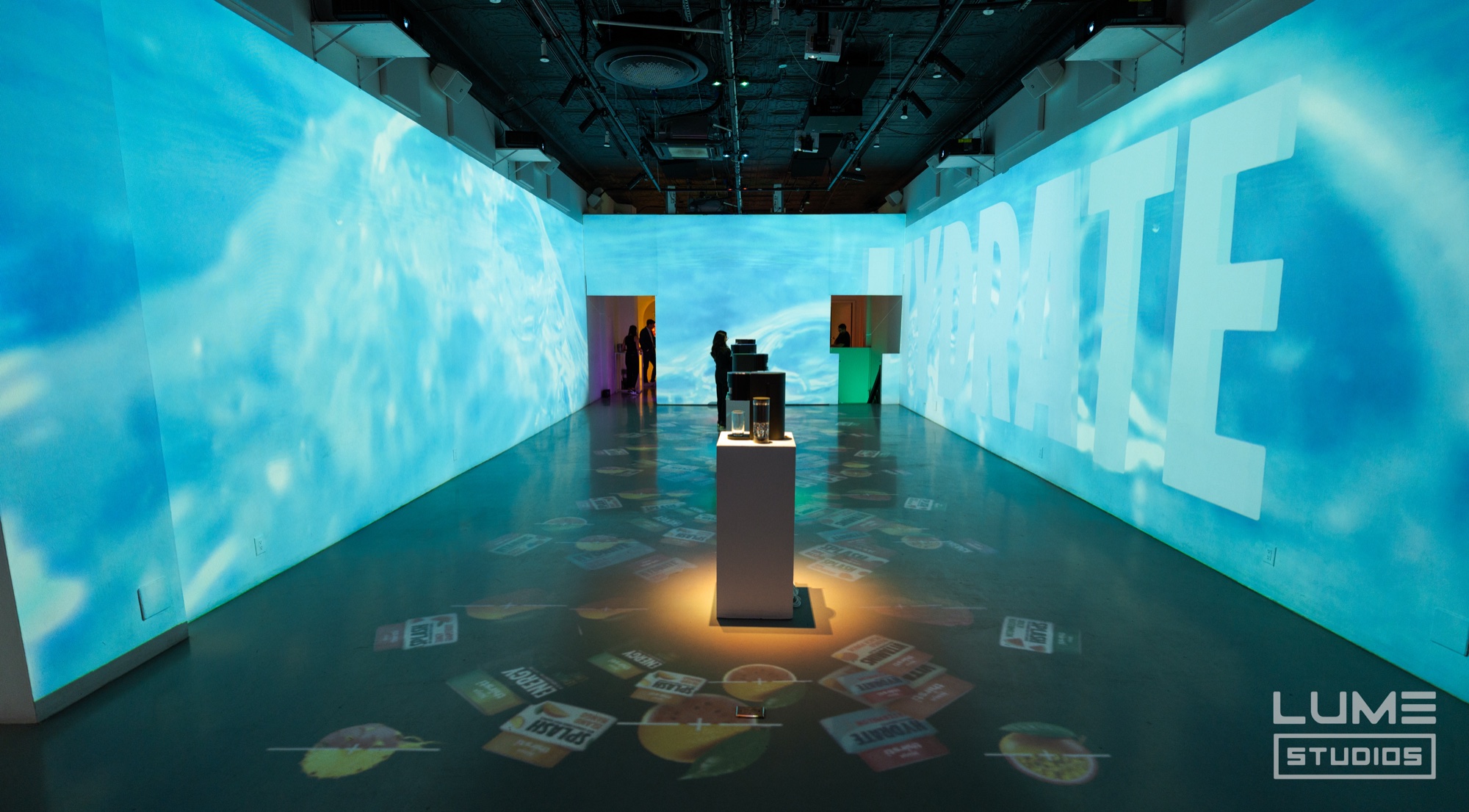 Guests mingle around a lit pedestal as green citrus visuals wash the Lume Studios walls