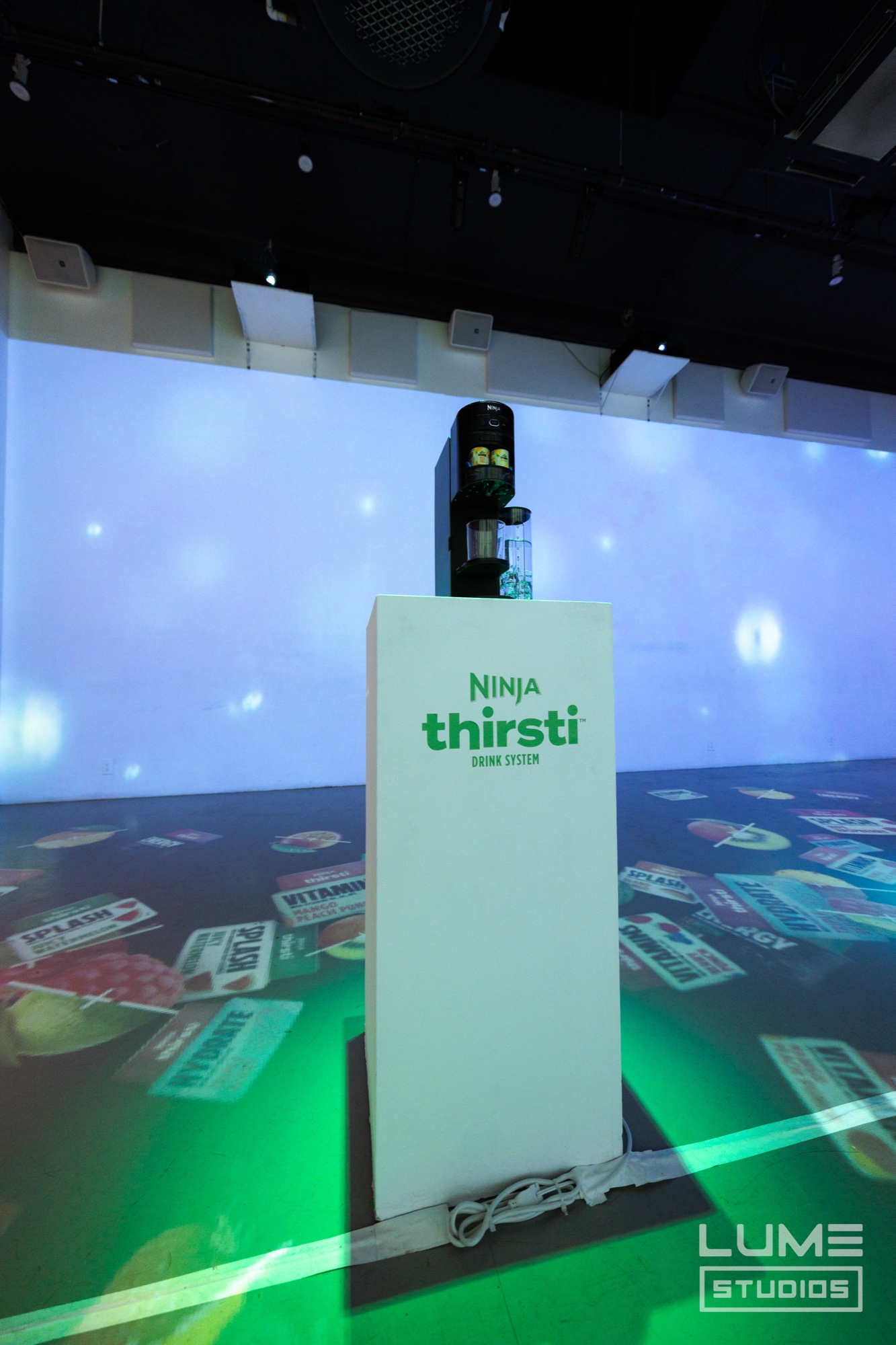 Ninja Thirsti drink machine on a white plinth in front of a wall projection of drifting flavour labels