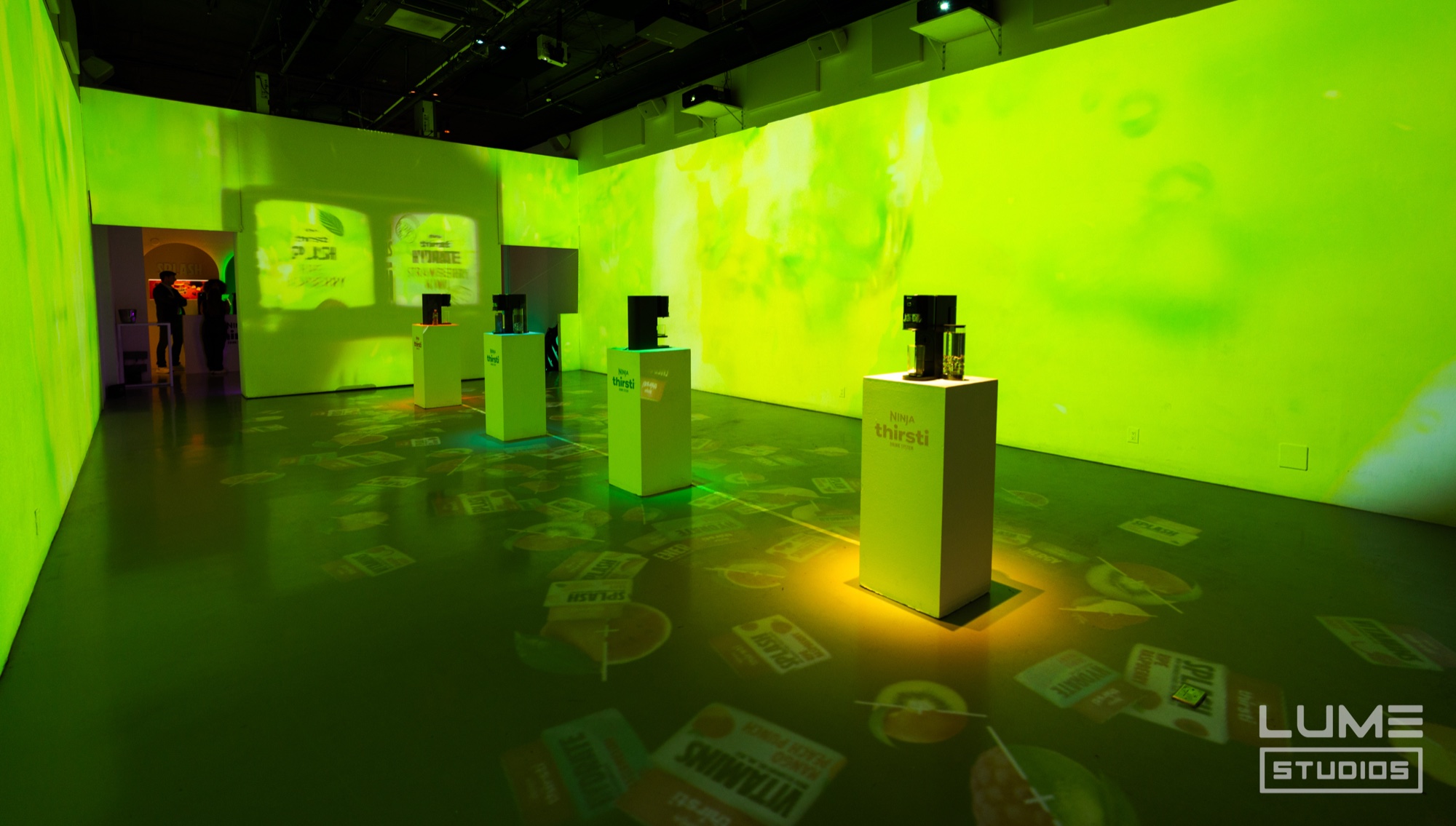 White pedestals stand on a floor scattered with projected labels in a room washed entirely in green light