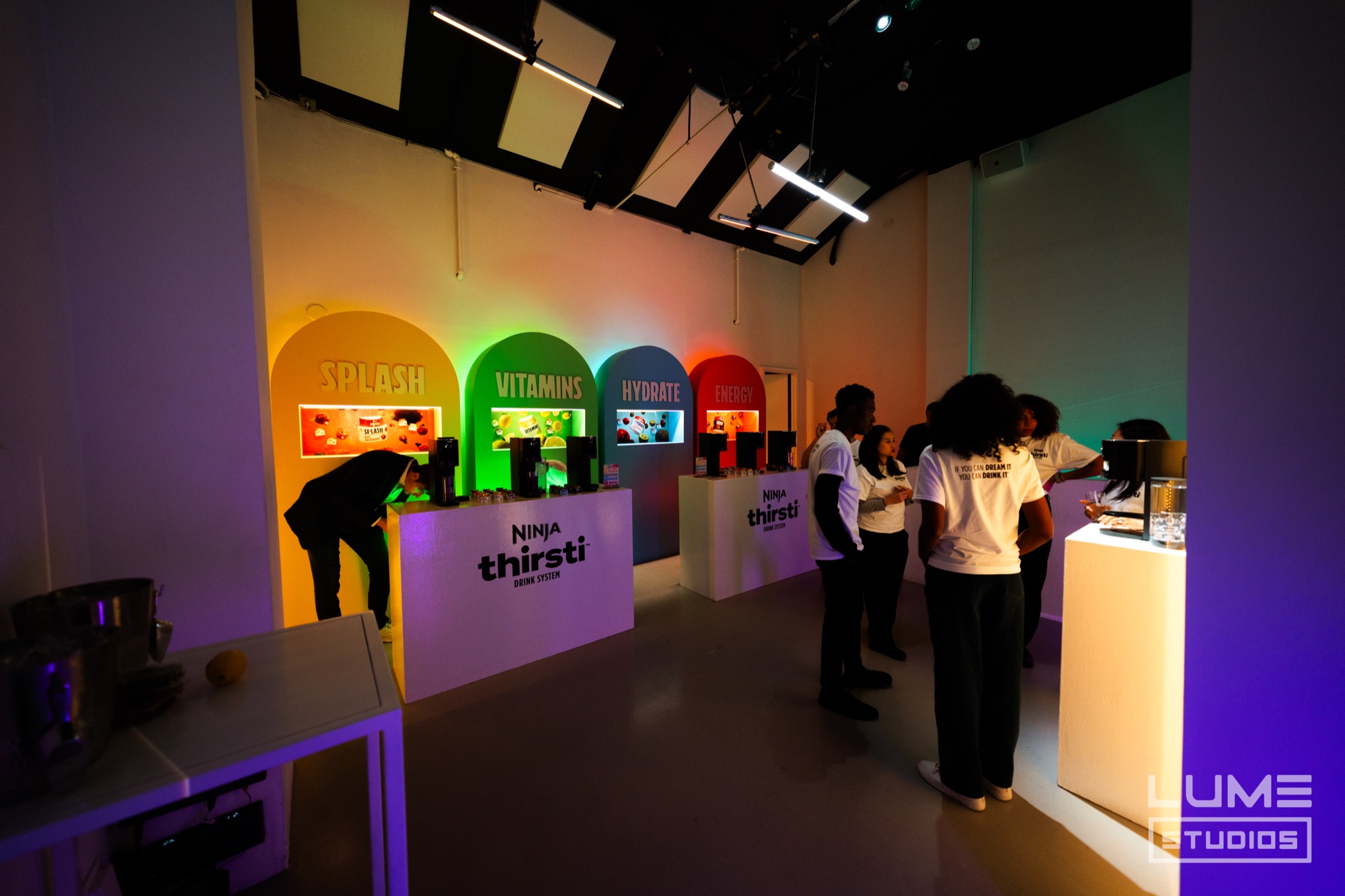 Guests sample drinks at a Ninja Thirsti counter with four arched displays labelled Splash, Vitamins, Hydrate and Energy