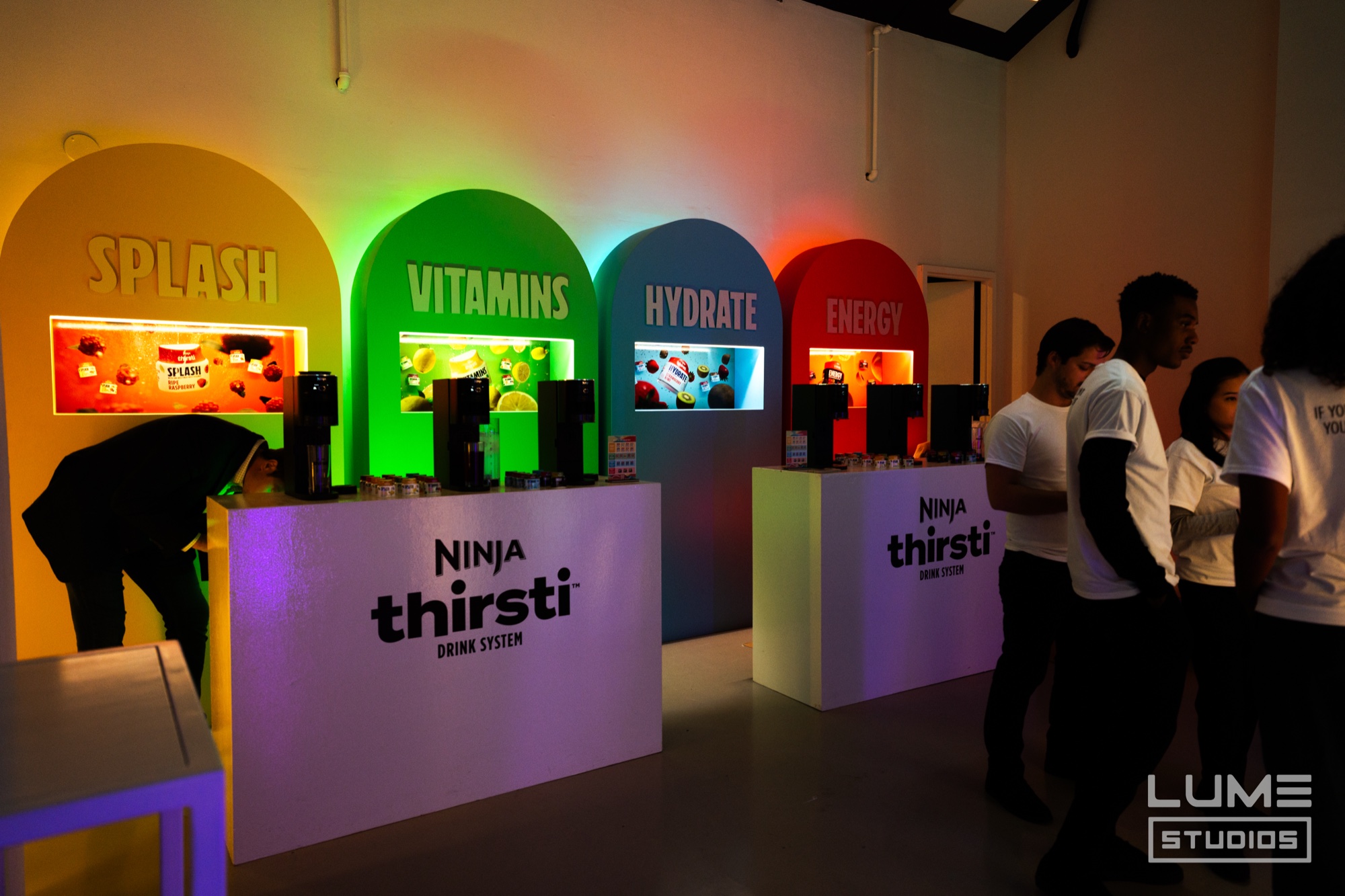 Four coloured arches labelled Splash, Vitamins, Hydrate and Energy above Ninja Thirsti counters as guests line up