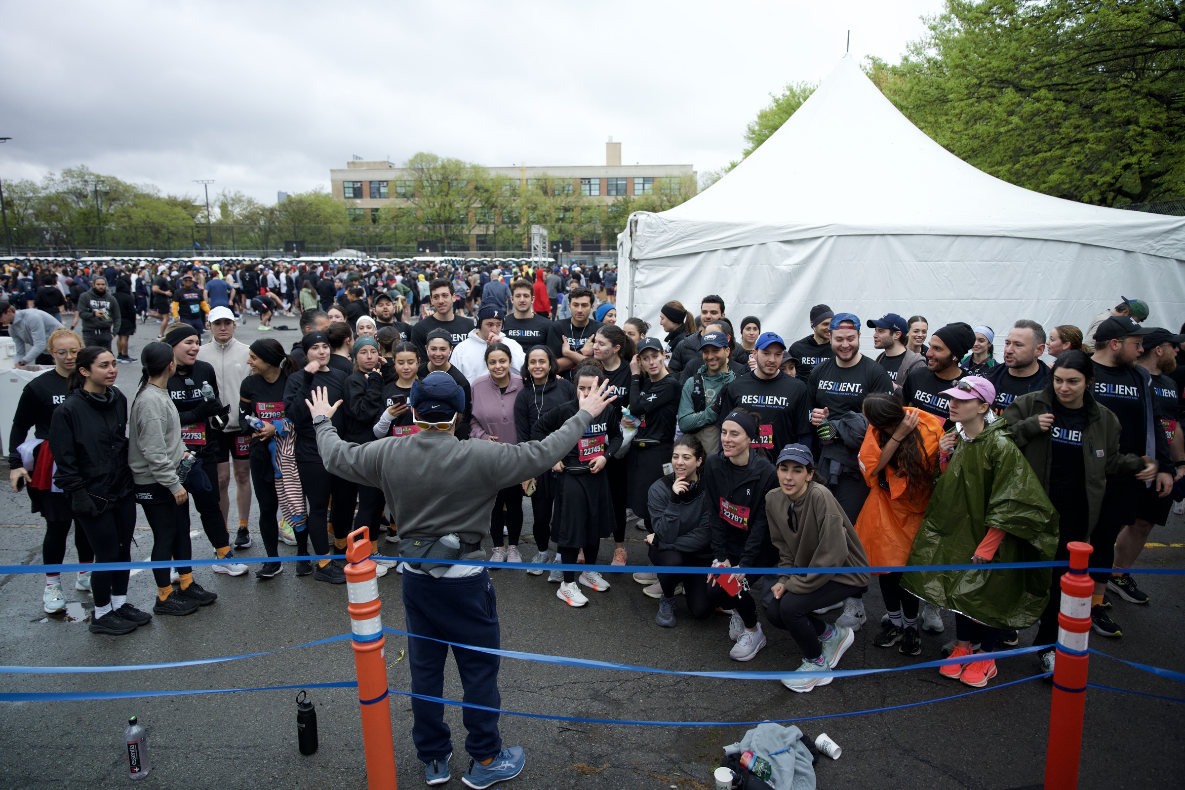 A large team gathered behind a blue rope at the start area, one person waving them together