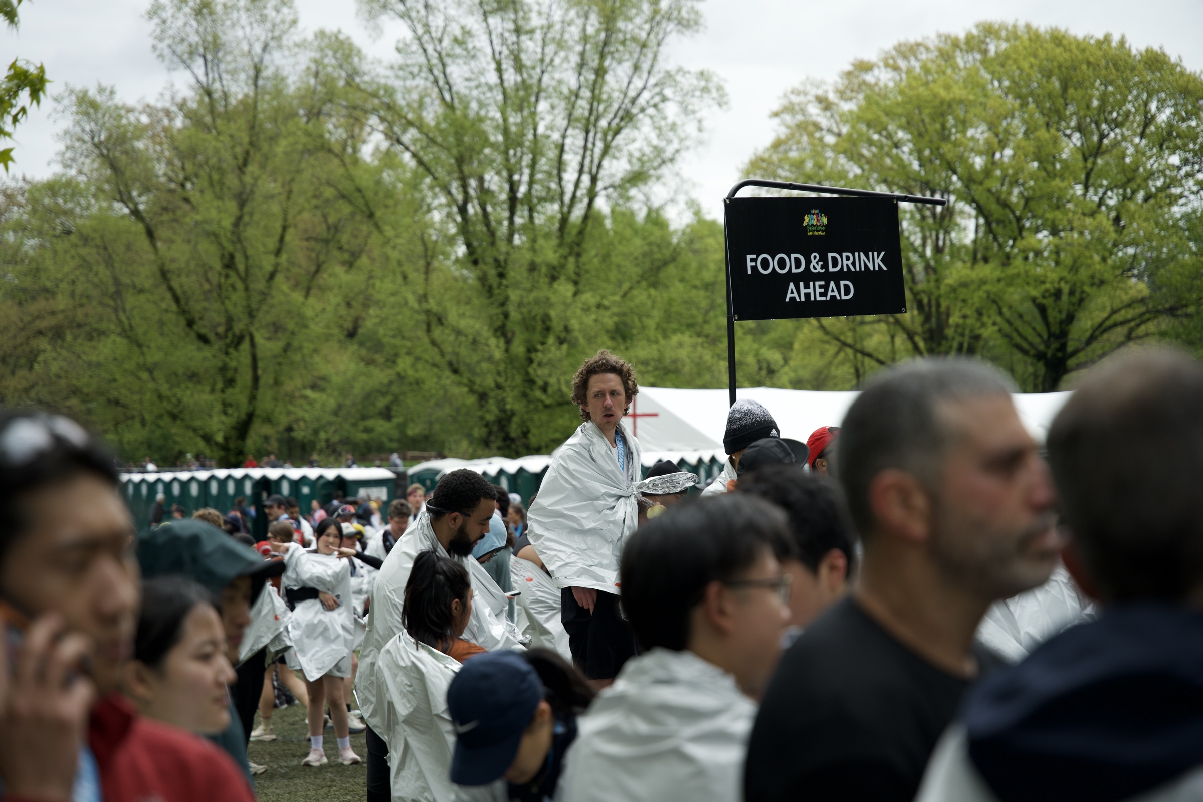 Runners in foil blankets moving past a black sign reading food and drink ahead