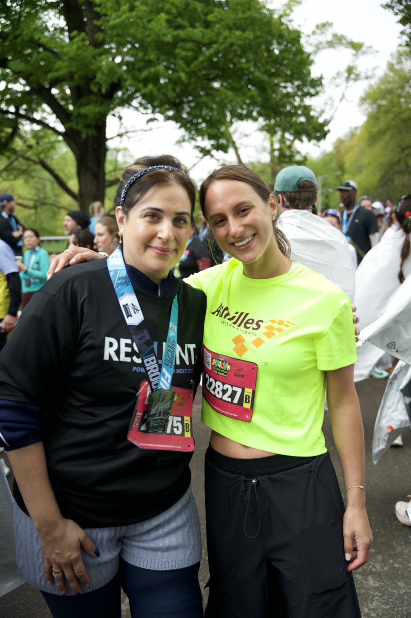 Two runners with finisher medals, one in a Resilient shirt and one in a yellow race shirt, under trees