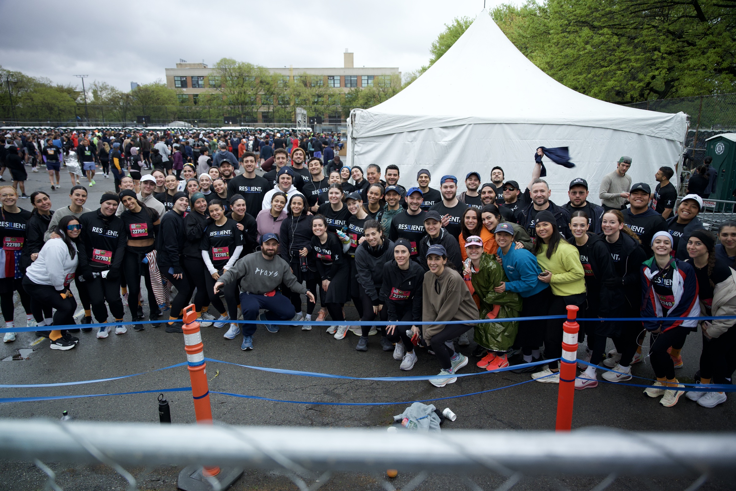 The whole team packed behind the rope before the start, grey sky over the tents
