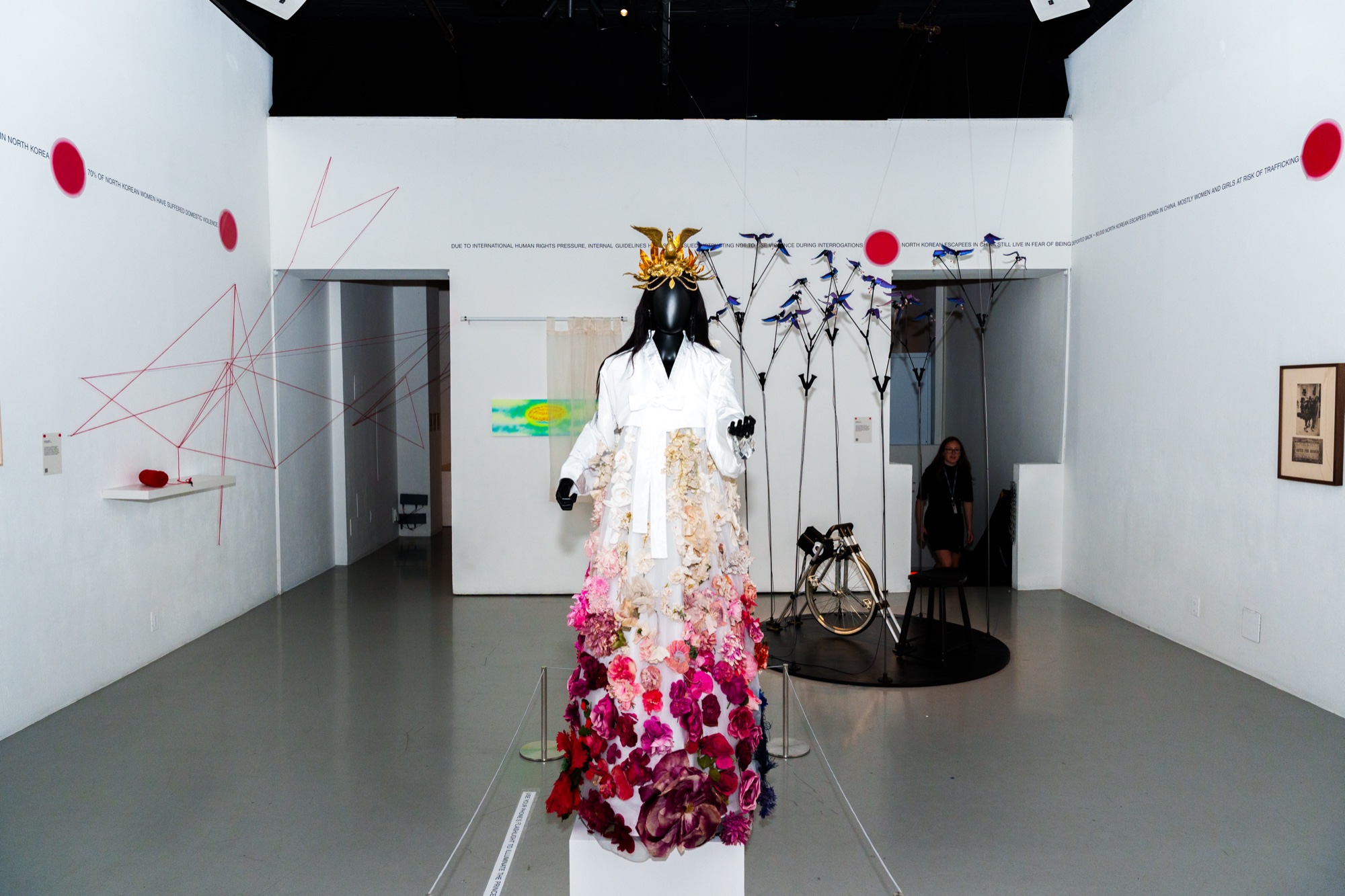 Mannequin in a gown of white to red flowers and a gold headdress in a white gallery with red dots