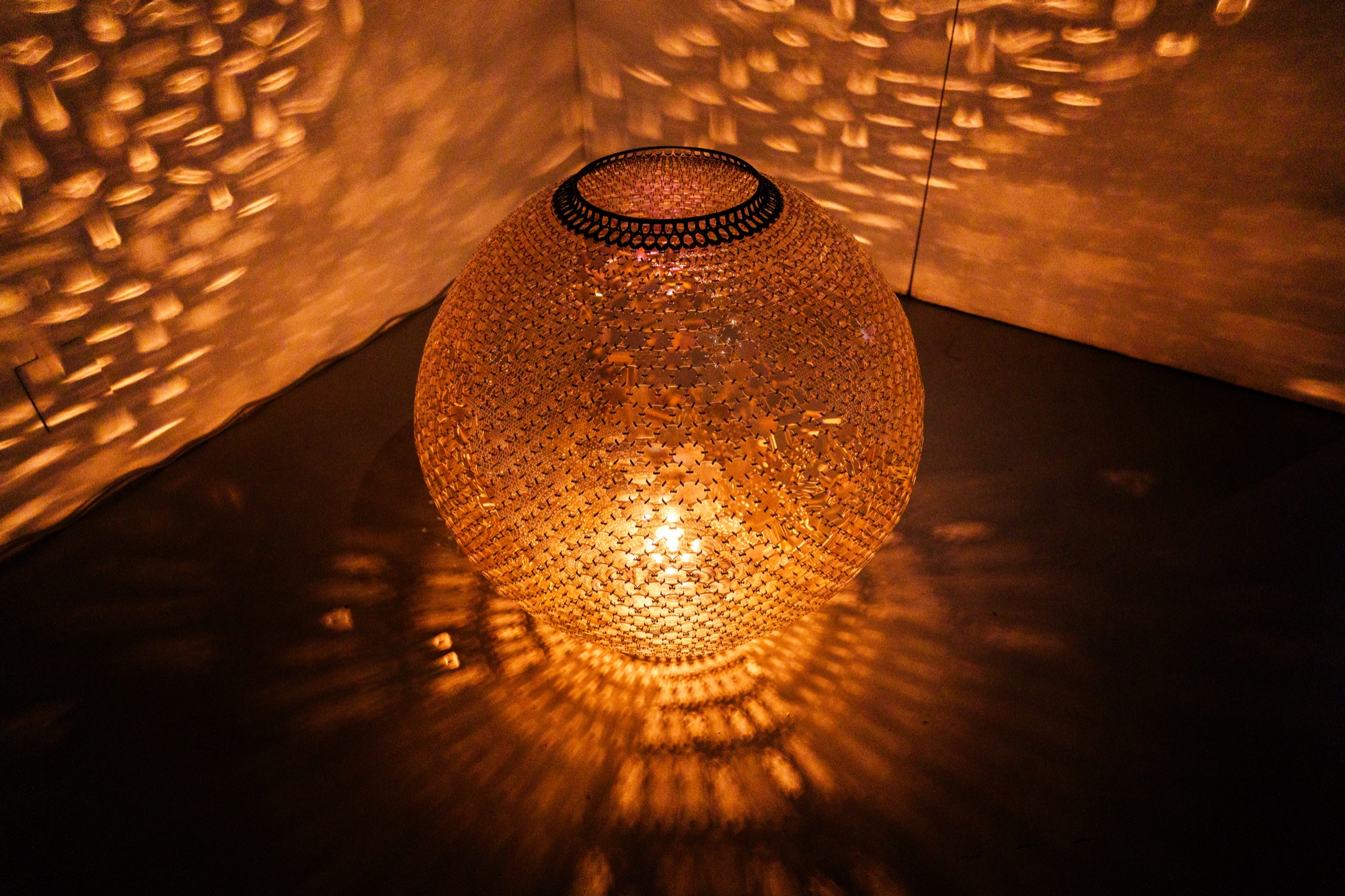 A glowing round lantern of pierced metal throws a lace of golden light across the surrounding walls