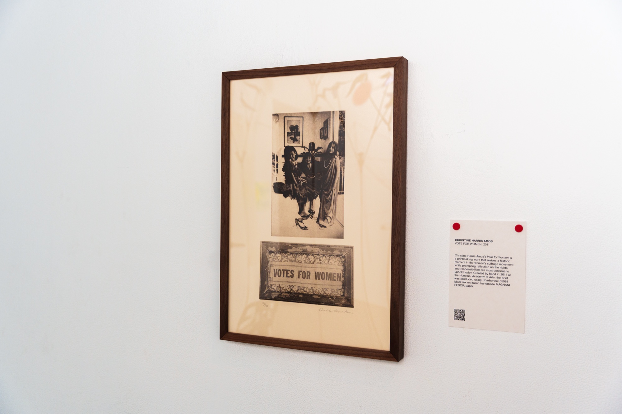 Framed sepia print of suffragettes above a votes for women sign hanging beside a wall label