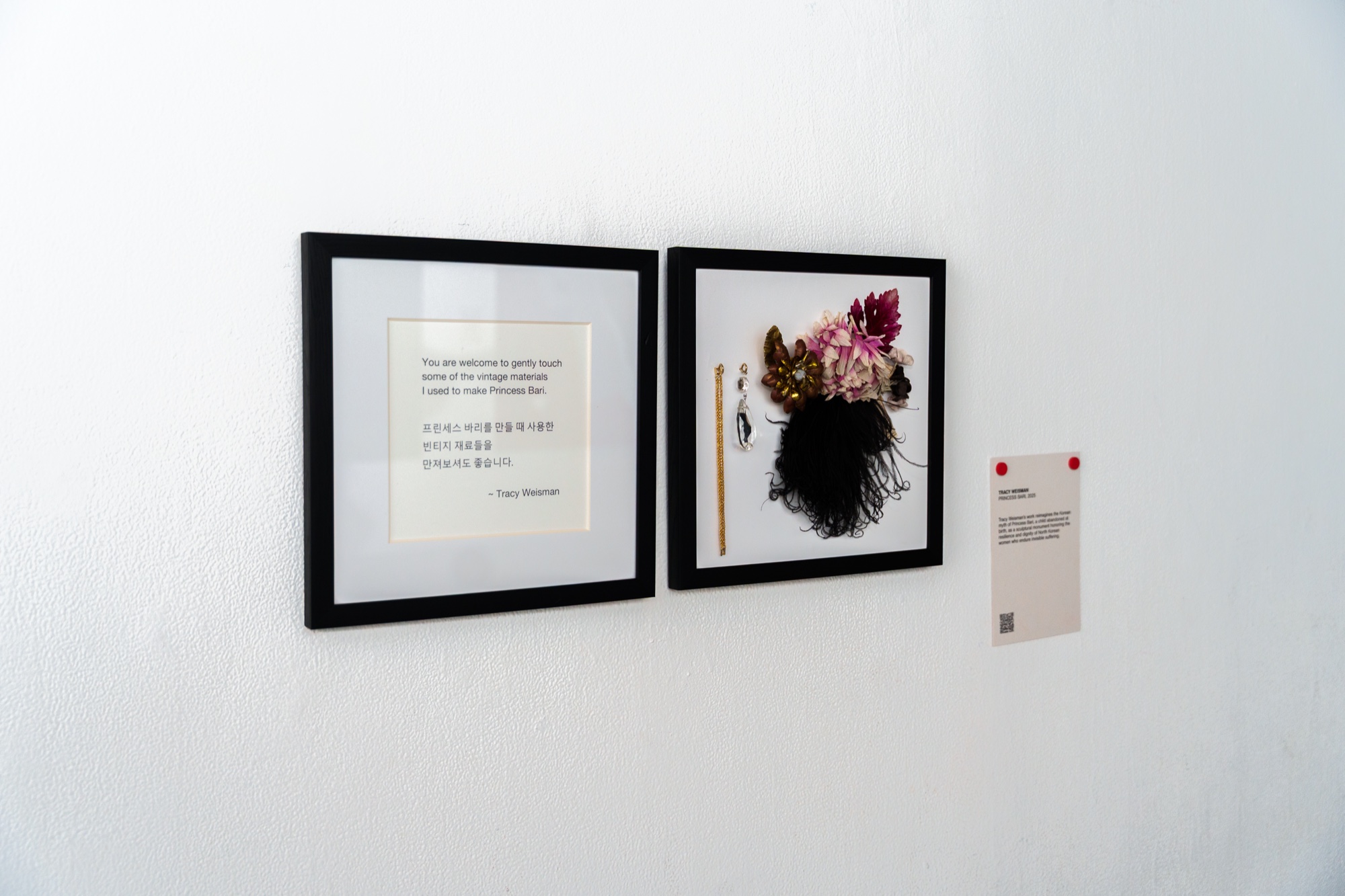Two black framed pieces on a white wall, a printed text panel and pressed flowers with a comb and tassel