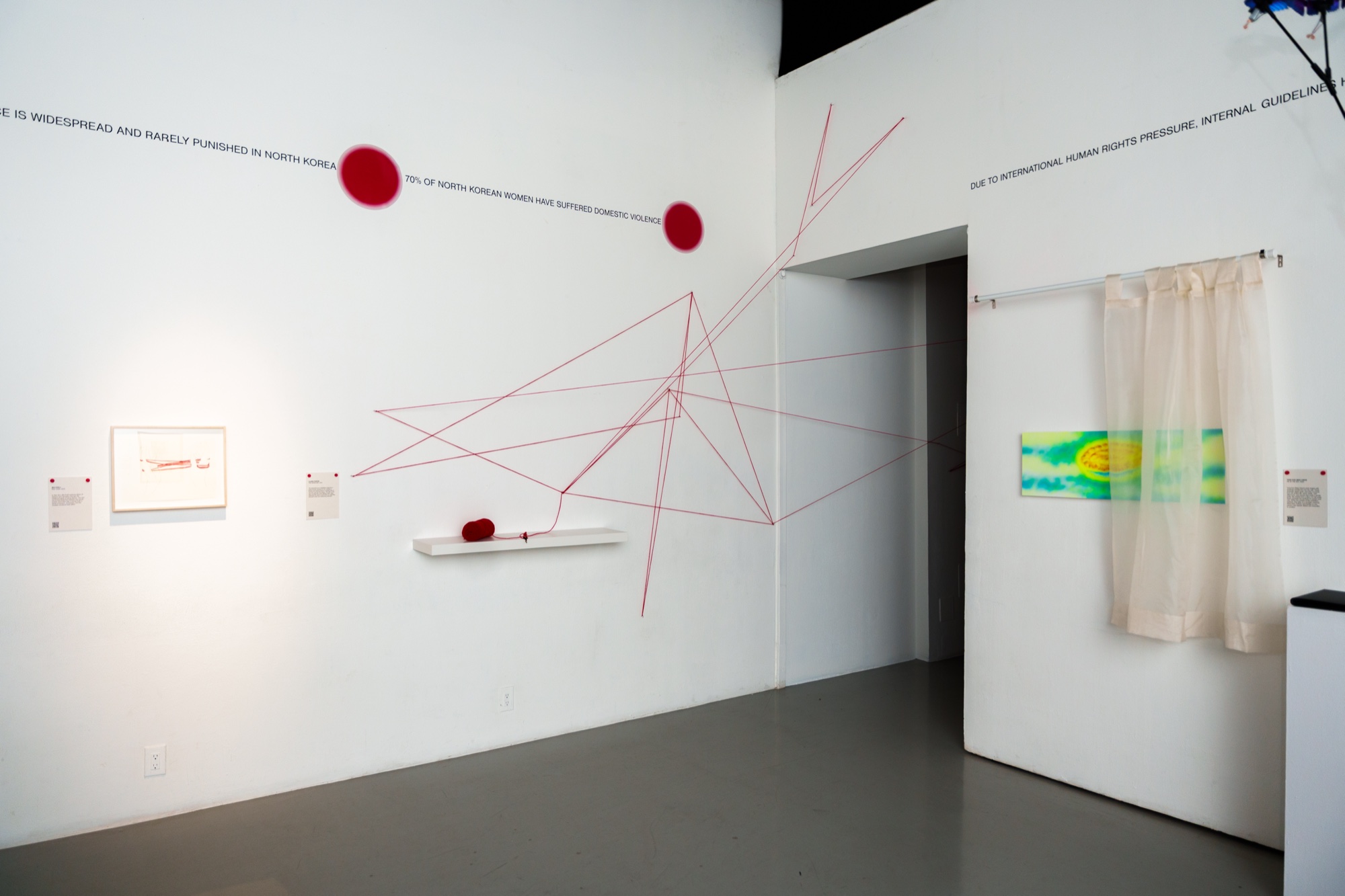 White gallery wall with red string stretched into lines, two red circles and a hanging sheer curtain