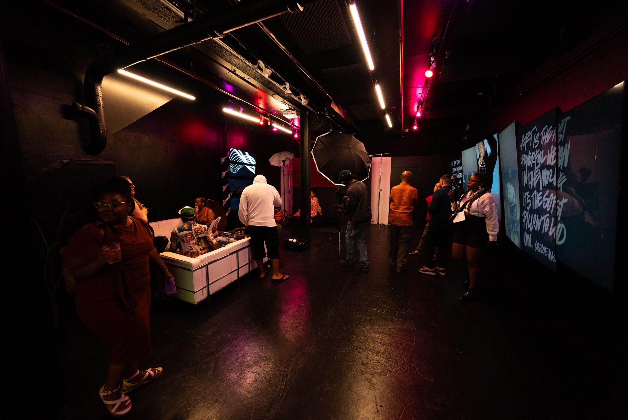 Guests move through a dark venue under pink and red light with white lettering projected on screens