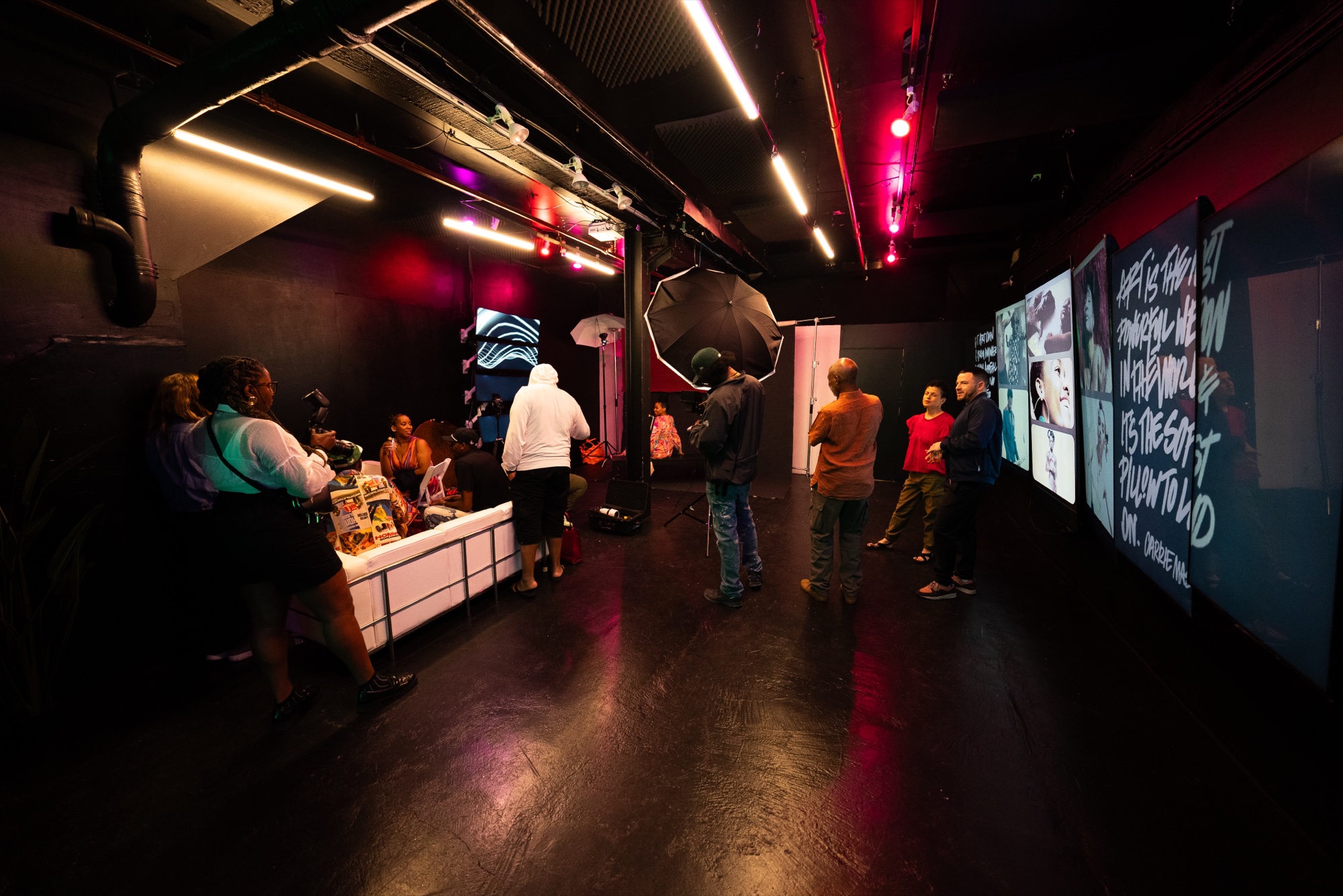 Guests in a dark red lit room near a photo booth umbrella light and screens of white handwritten text