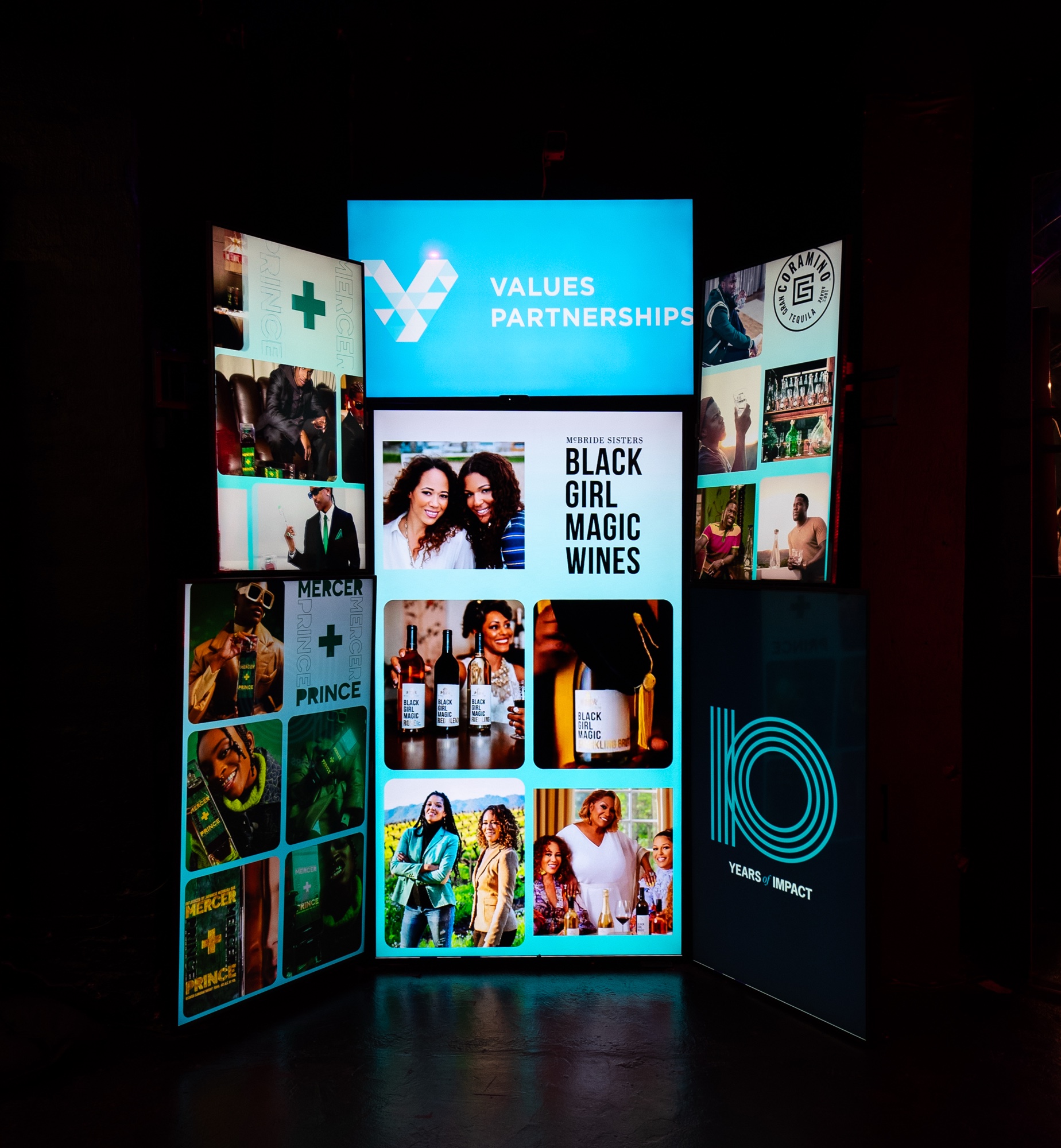 Illuminated column of screens showing a Values Partnerships logo, Black Girl Magic Wines and a 10 Years panel