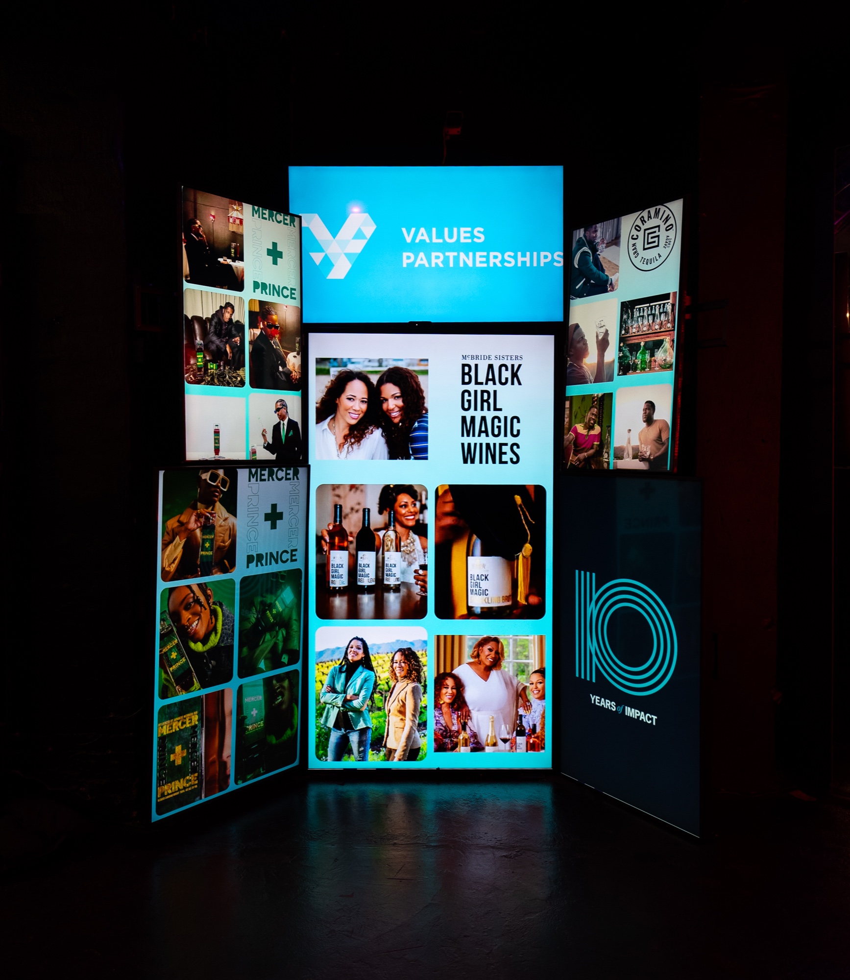 Glowing three panel display reading Values Partnerships with photo tiles and a Black Girl Magic Wines poster