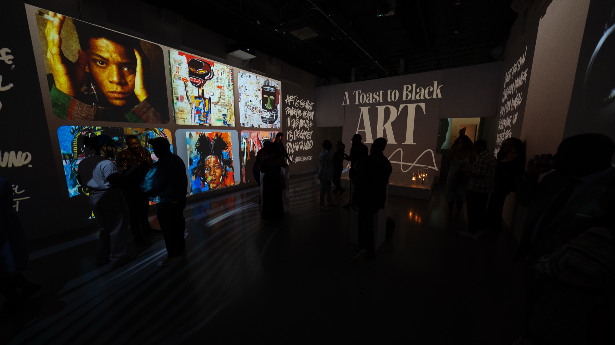 Guests walk past projected portraits and street art beneath the words A Toast to Black Art on a dark wall