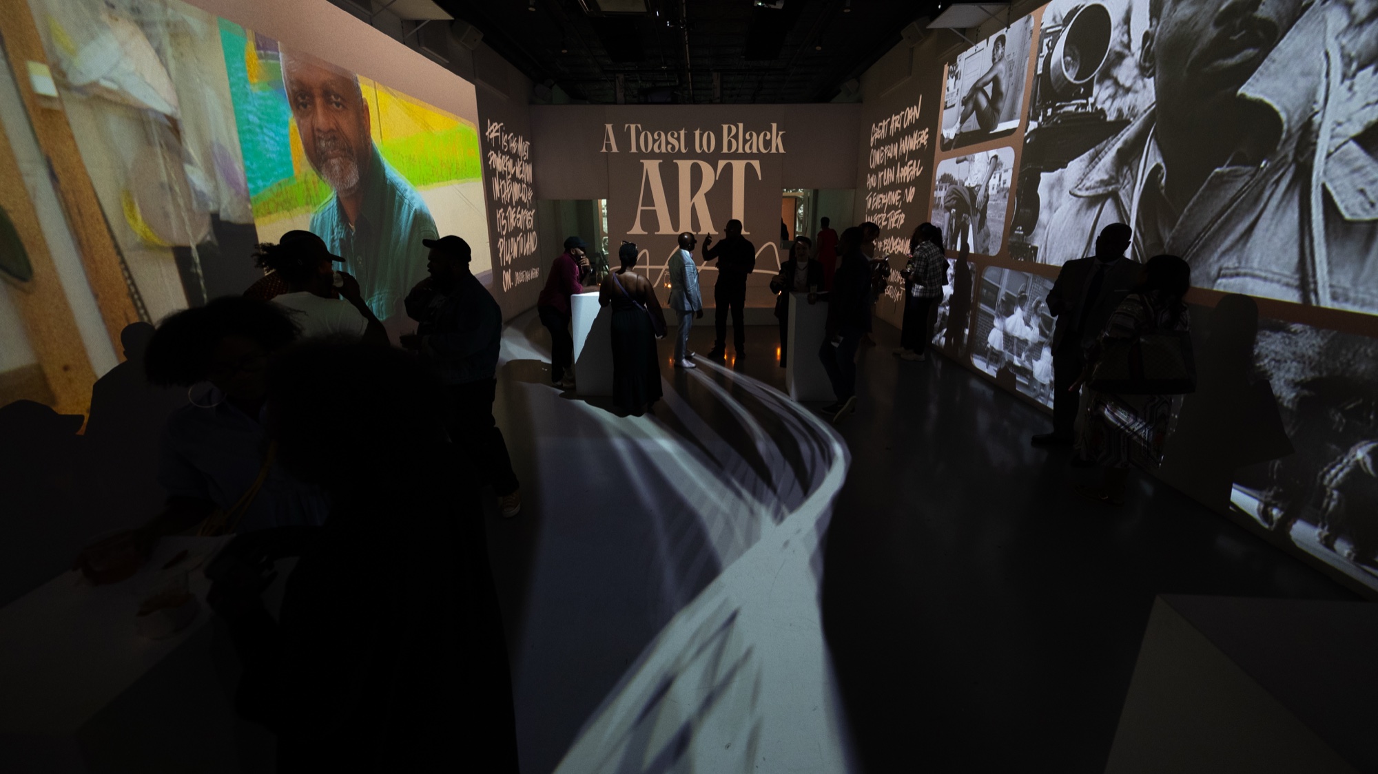 Guests gather beneath A Toast to Black Art projected on the far wall, flanked by black and white portraits