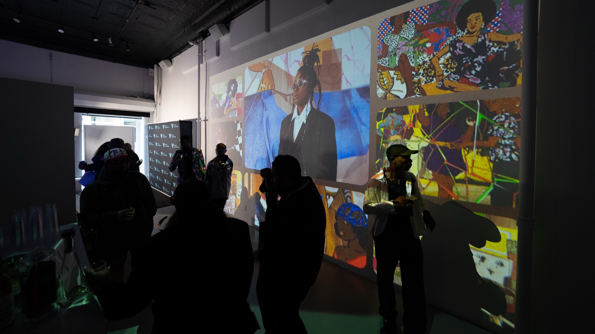 Silhouetted crowd faces a wall projected with collage portraits and a figure in a dark suit