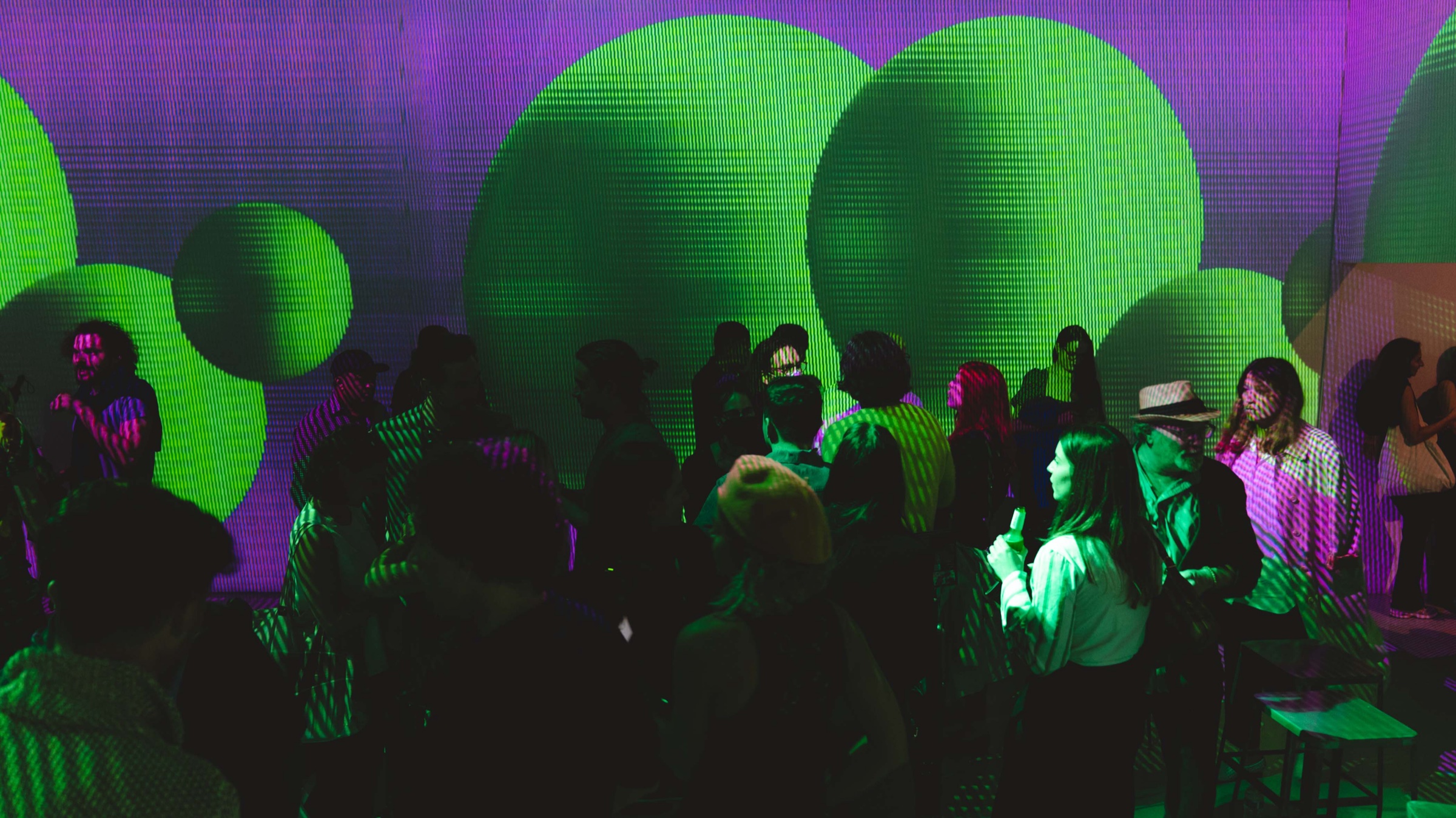 Party crowd silhouetted against green and purple projections at the Vertical Crypto Art event