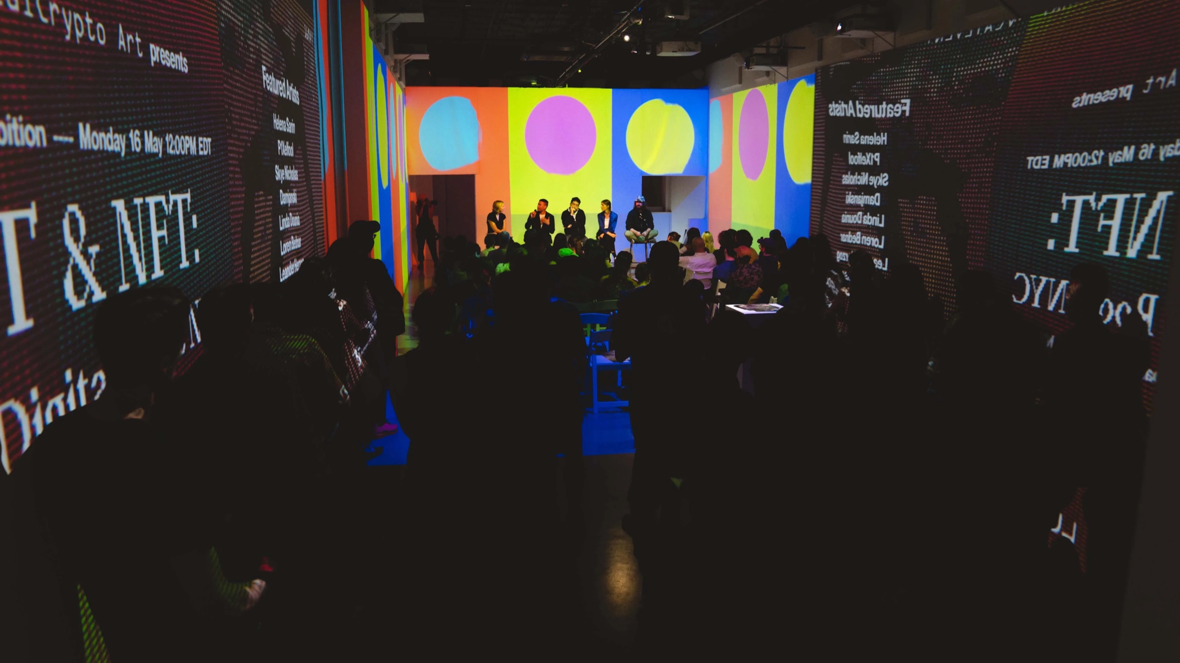 Crowd under colorful projections announcing Art and NFT at Vertical Crypto Art