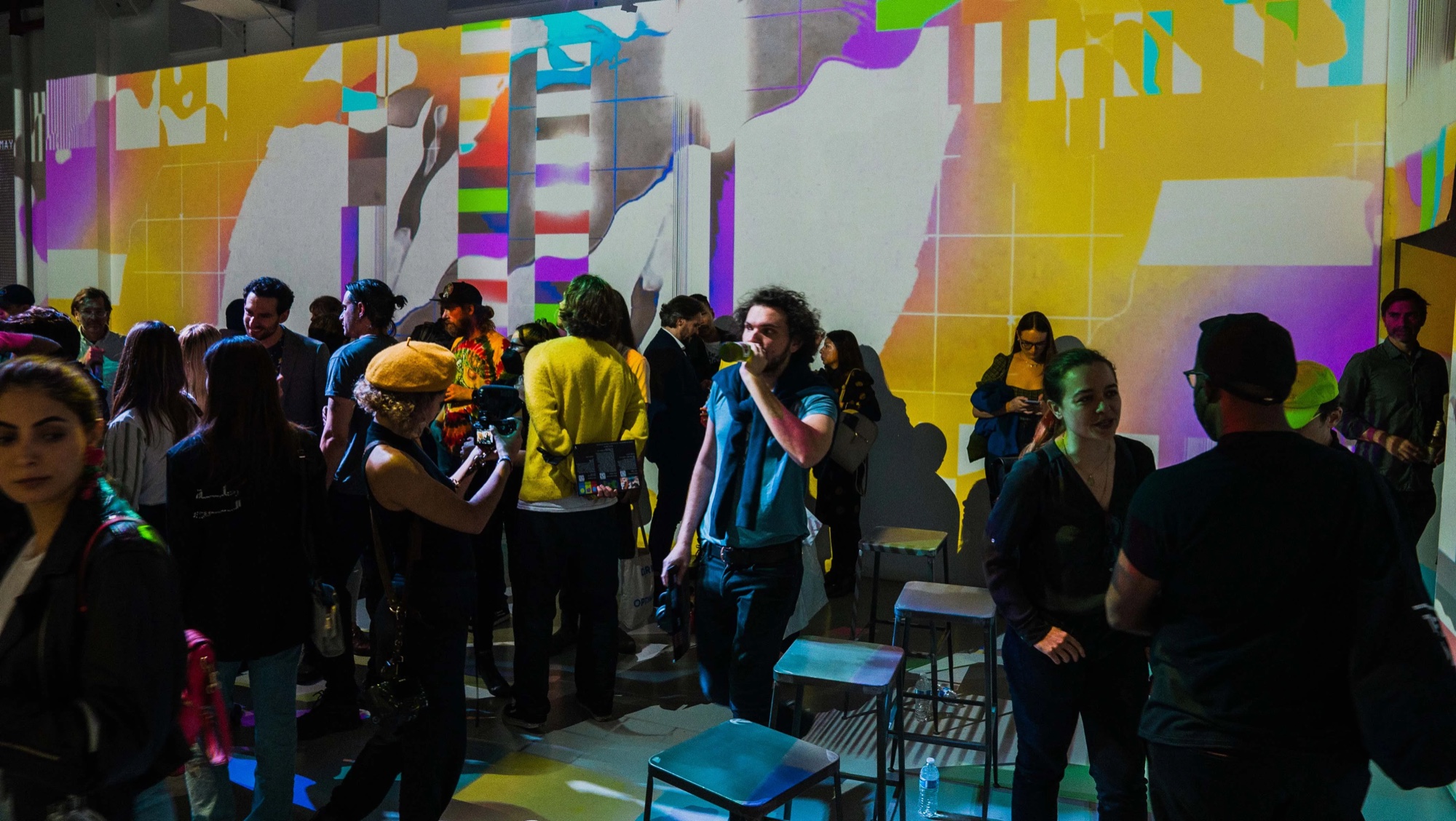 Guests in front of yellow and purple abstract wall projections at Vertical Crypto Art