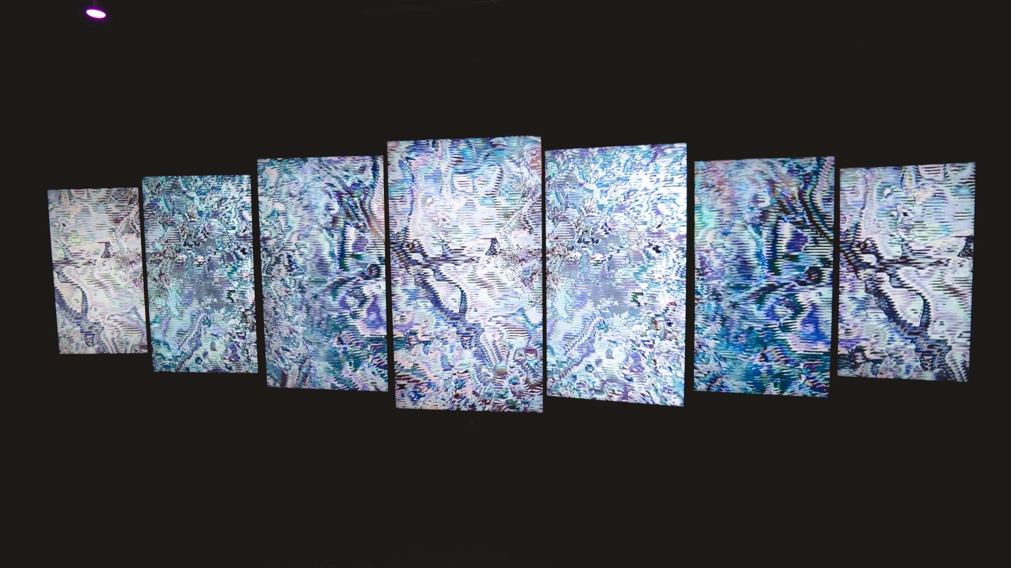 Row of angled screens showing silver abstract art in a dark room