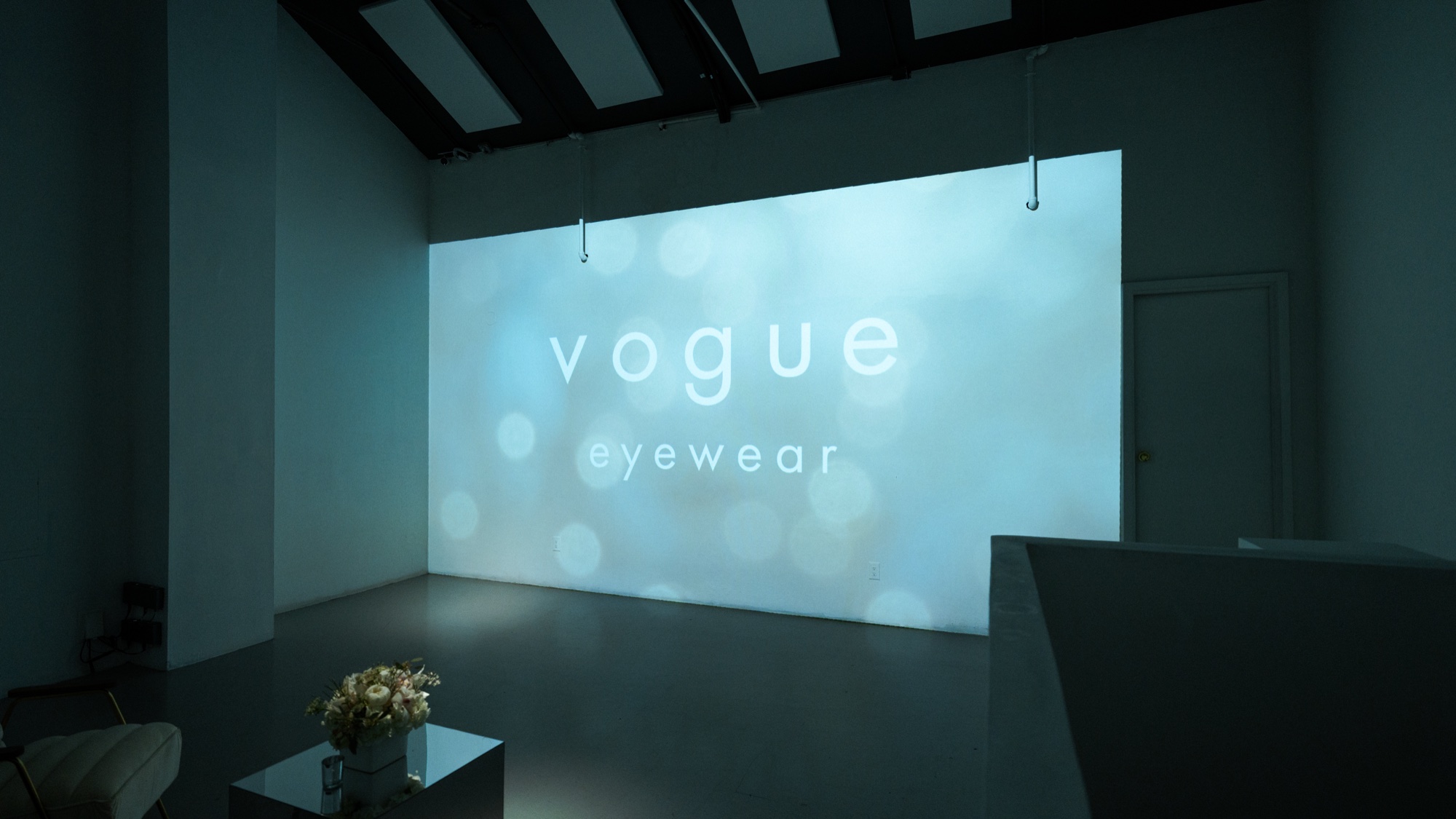 Crowd mingles beside flower arrangements in the red lit Vogue Eyewear room