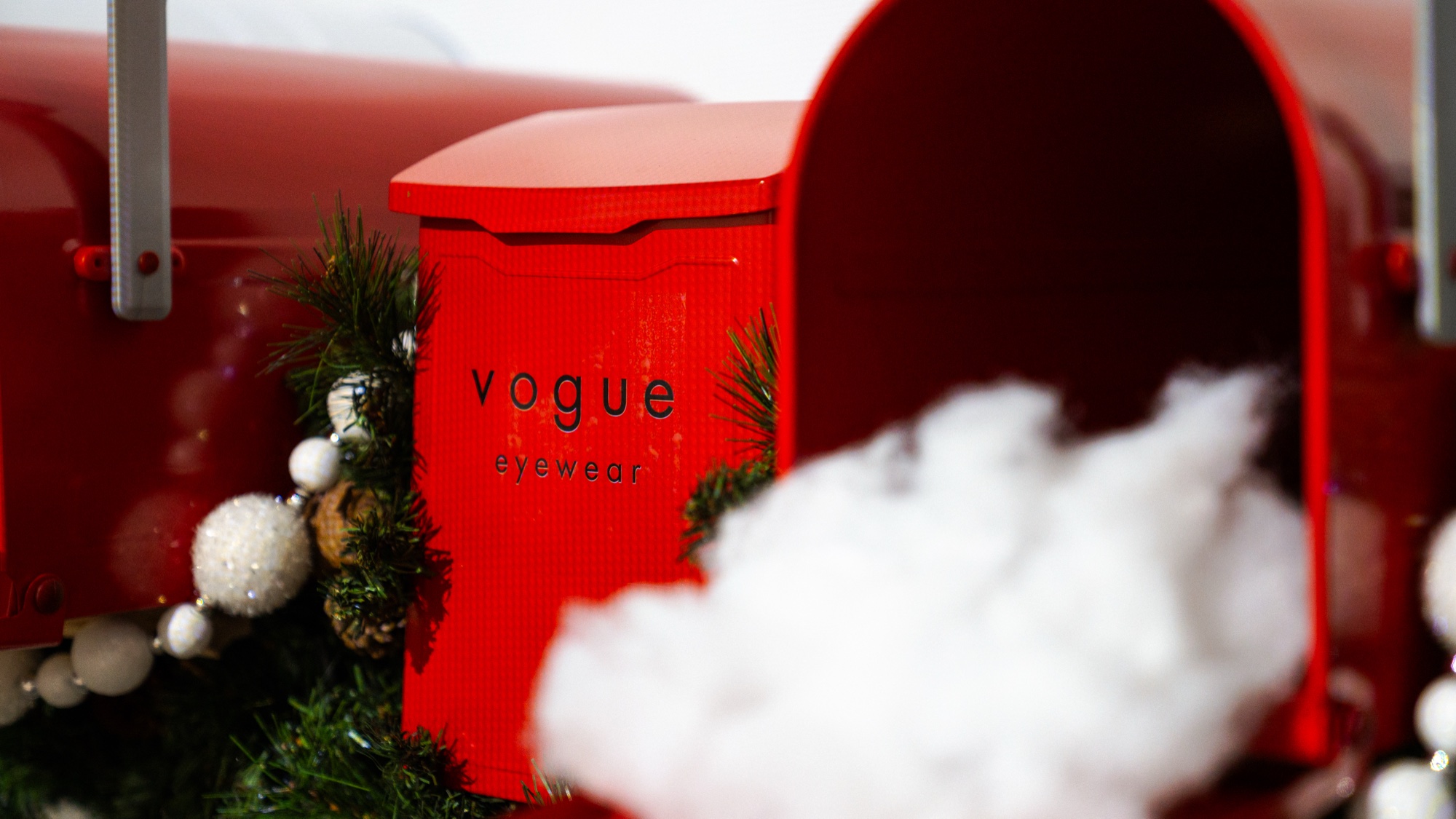 A red mailbox printed with Vogue Eyewear sits among fake snow and pine garland with white baubles