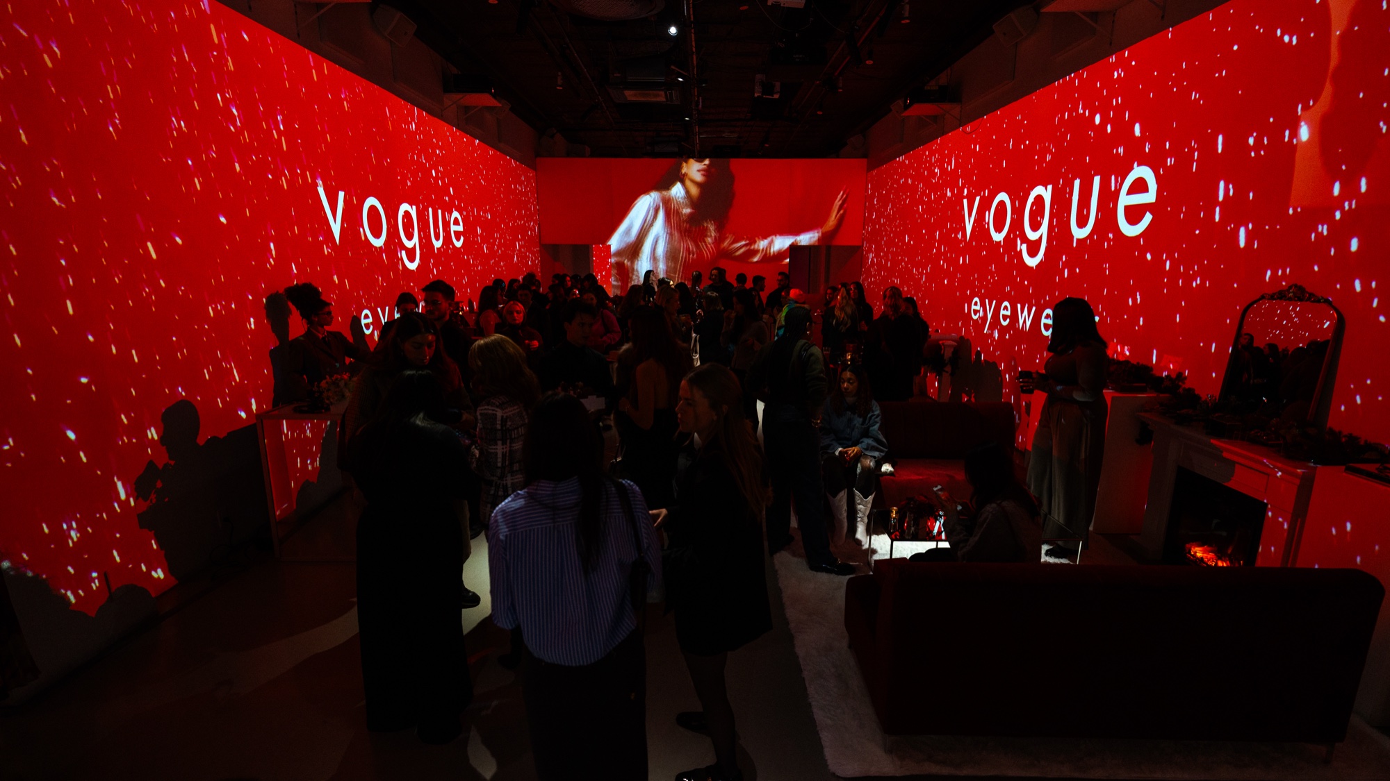 Guests mingle in a red lit room with Vogue Eyewear on the walls and a projected figure at the end
