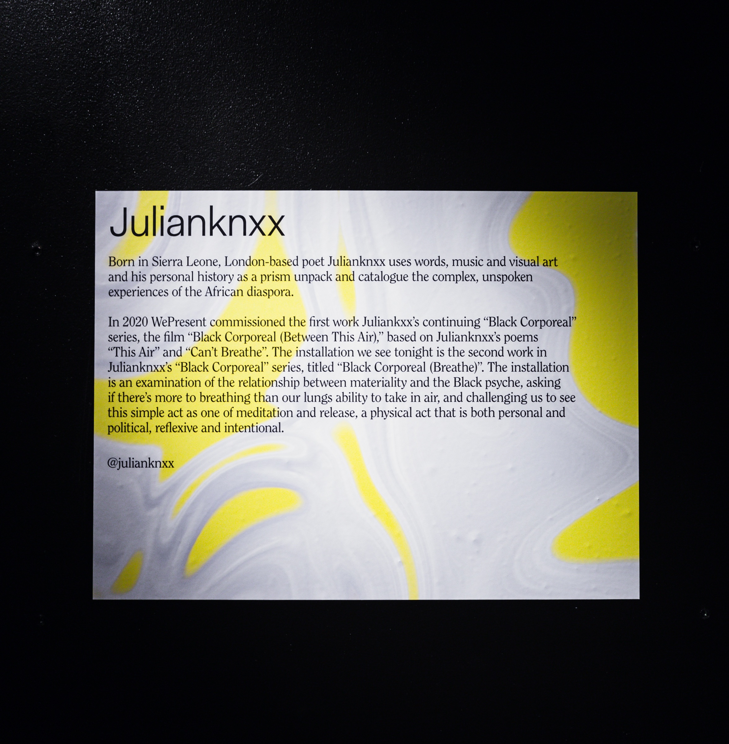 White placard with yellow marbling introduces the poet Julianknxx against a black wall