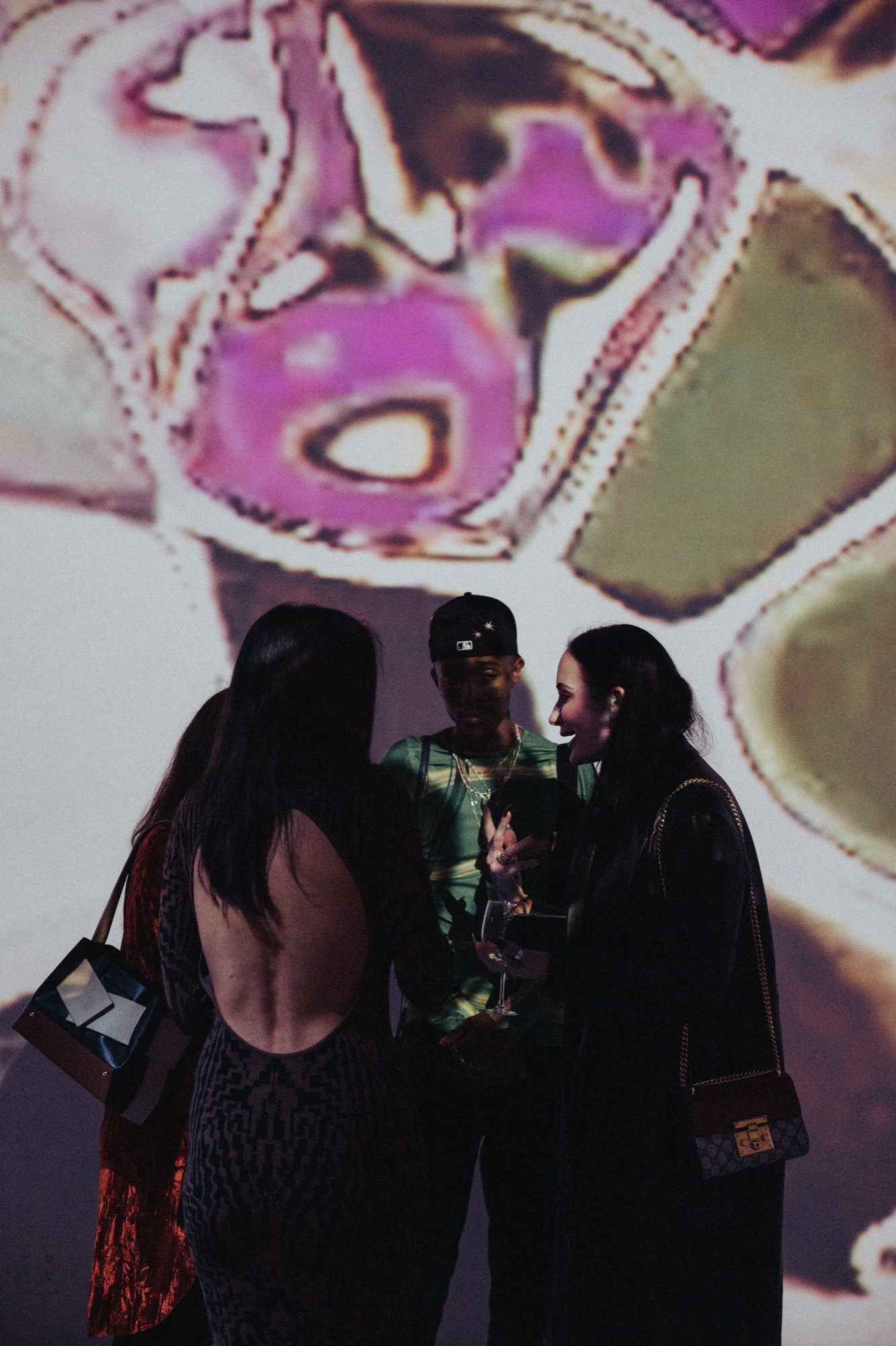 Three guests in silhouette chat with glasses beneath a magenta and green abstract projection
