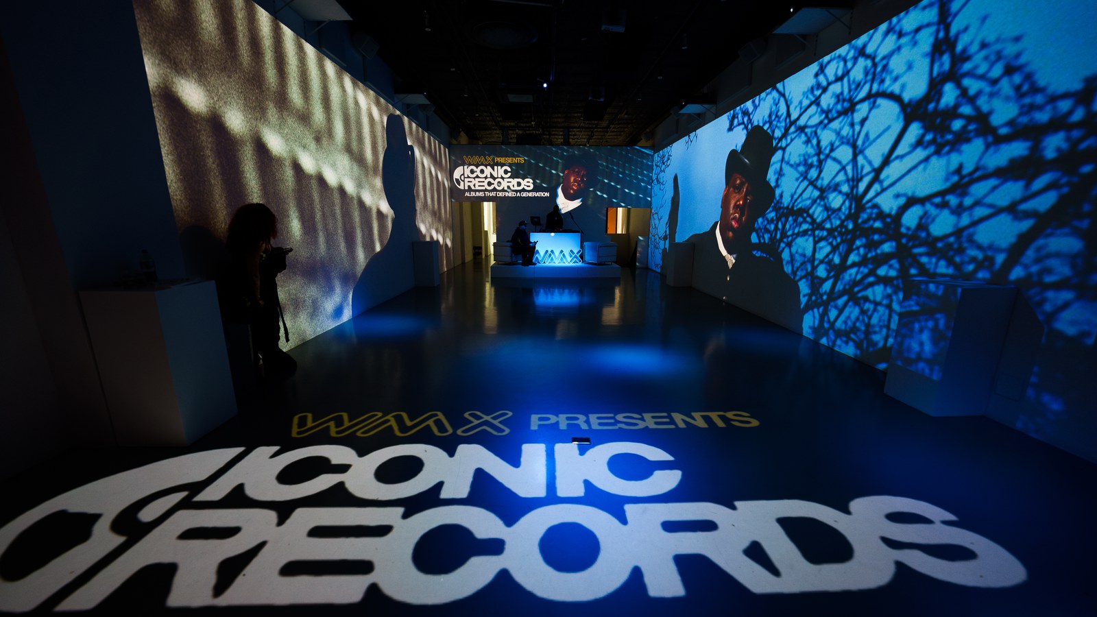 WMX Presents Iconic Records projected on the floor of a blue lit corridor with portraits on the walls