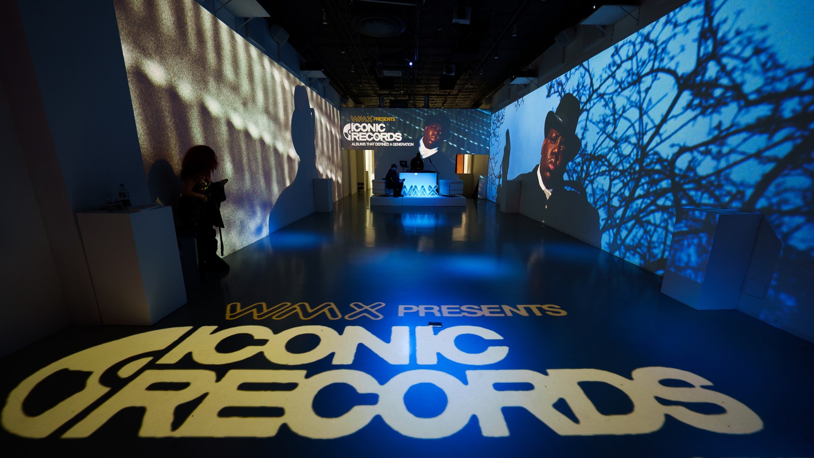 WMX Presents lettering projected in yellow on the floor of a dark hall lined with blue photo projections