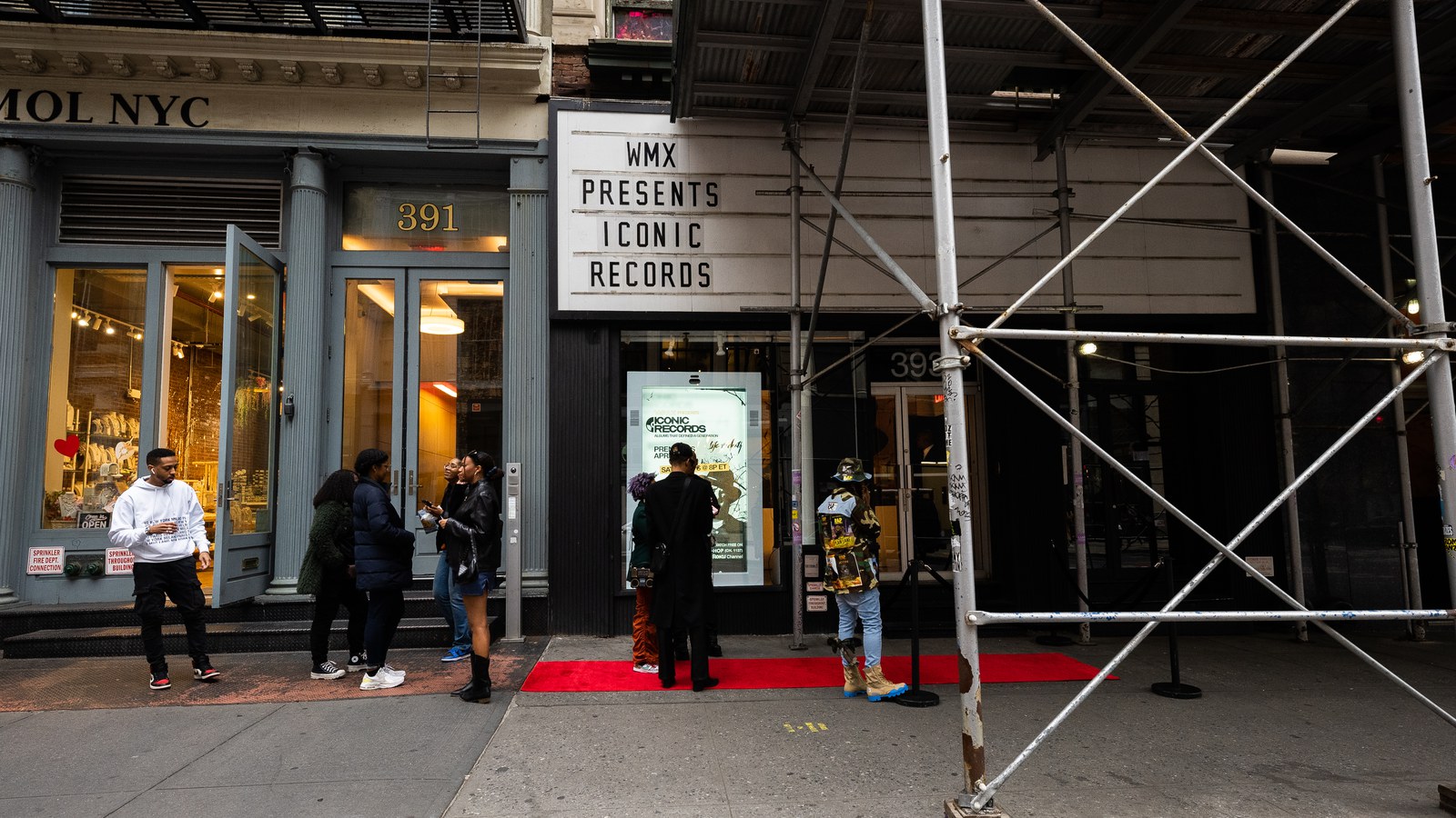 Storefront marquee announcing WMX Presents beneath scaffolding, red carpet at the door and guests waiting outside