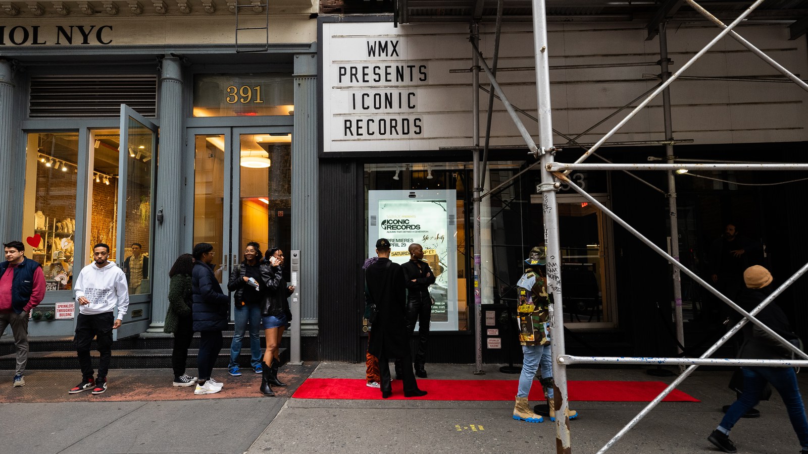 Marquee reading WMX Presents above a red carpet where a guard checks guests outside a cast iron storefront