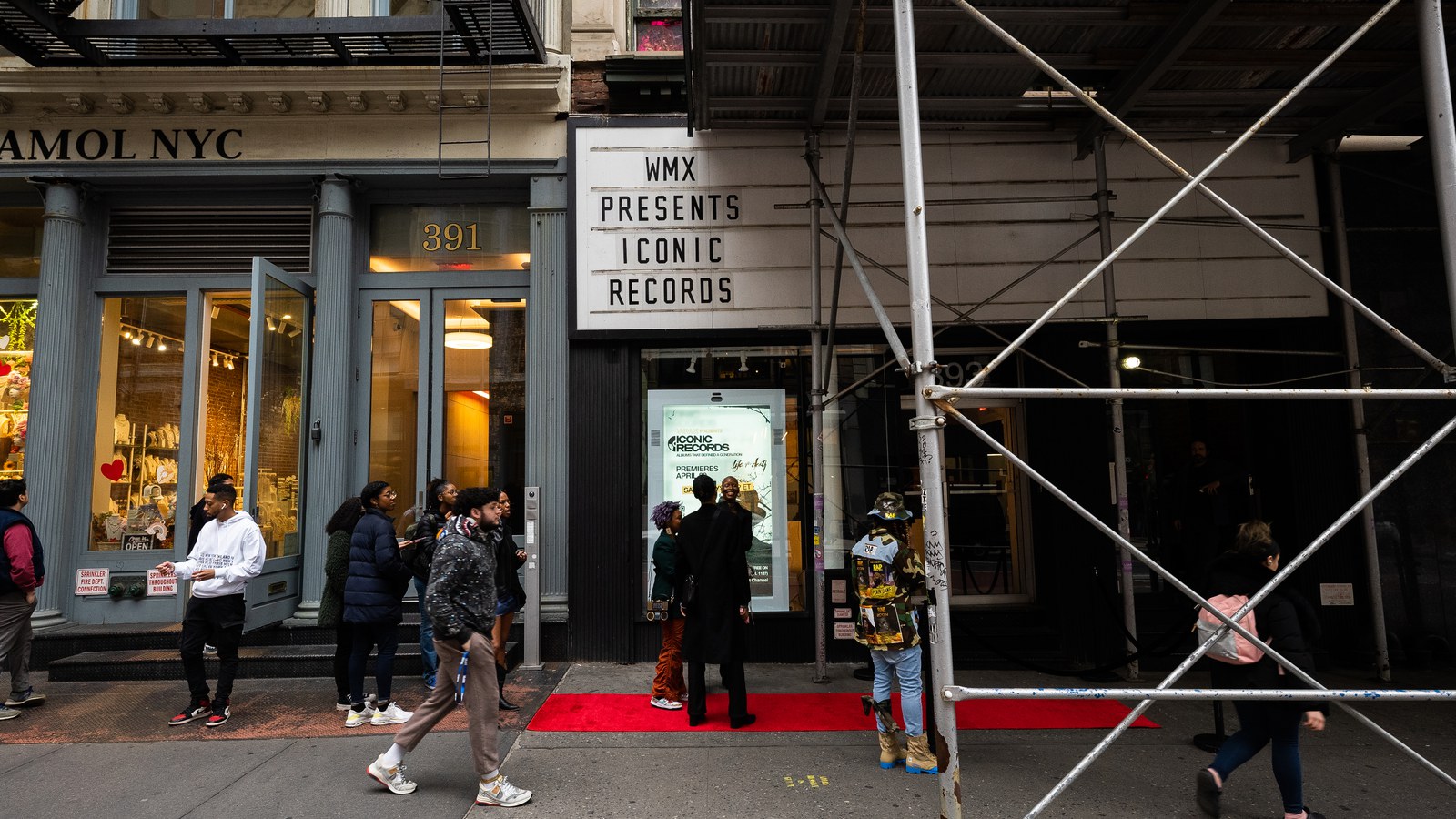 Red carpet leads into a storefront under a marquee reading WMX Presents Iconic Records beside green scaffolding